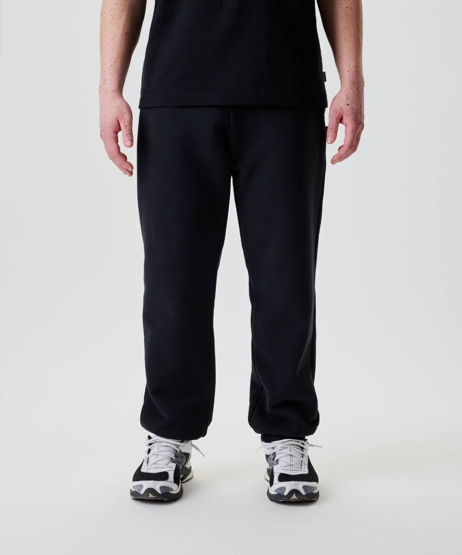 Person trägt Nays Classic Sweatpants mit elastischen Bündchen. Sichtbar sind YKK Reißverschlusstaschen und ein Teil des schwarzen T-Shirts über dem Hosenbund.