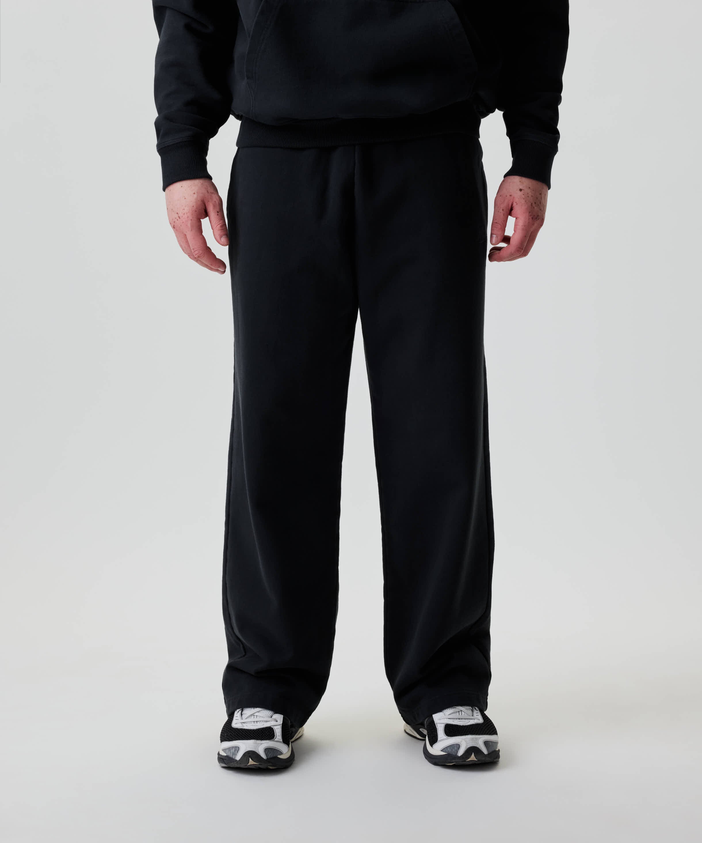 Person trägt Nays Straight Leg Sweatpants mit weitem Bein und sichtbarem Bund, kombiniert mit schwarzen und weißen Laufschuhen.