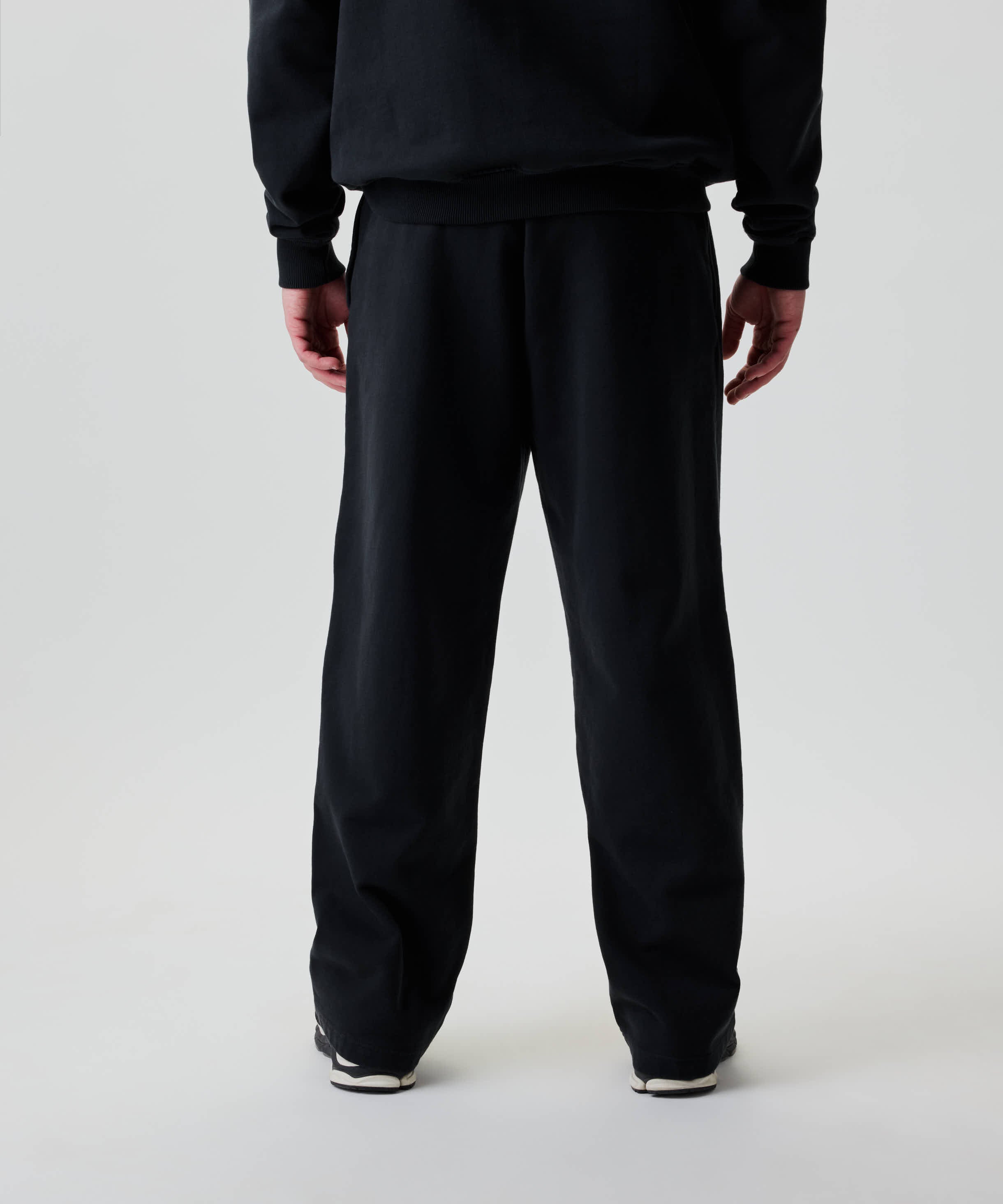 Person von hinten in Nays Straight Leg Sweatpants mit geradem, weitem Bein. Taschen mit YKK Zippern und kleiner Stickerei sind sichtbar.