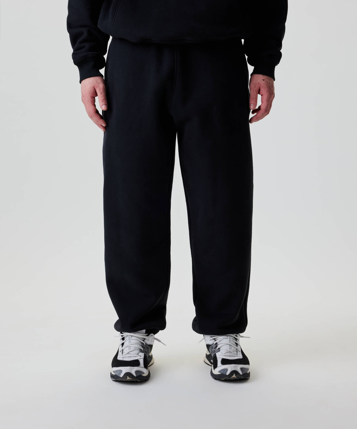 Person trägt Nays Baggy Sweatpants, locker geschnitten, mit praktischem Zipper-Taschen. Sichtbar sind auch klobige Sneakers, die entspannte Lässigkeit des Outfits unterstreichen.