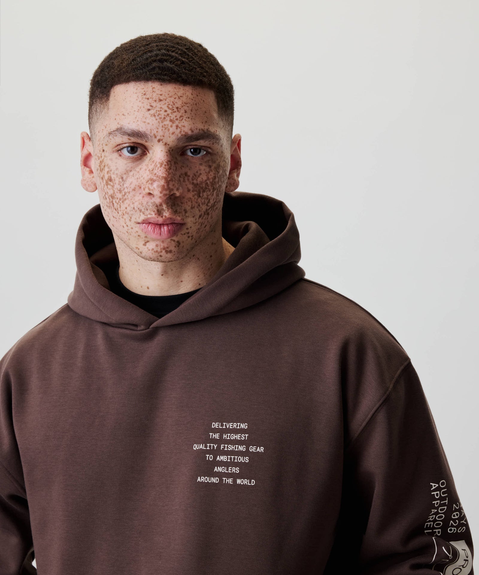 Junger Mann im Nays Quote Hoodie mit auffälligem Off-white-Text über Angelbedarf, komfortablem Baumwoll-Polyester-Mix und Fleece-Innenseite für täglichen Tragekomfort.