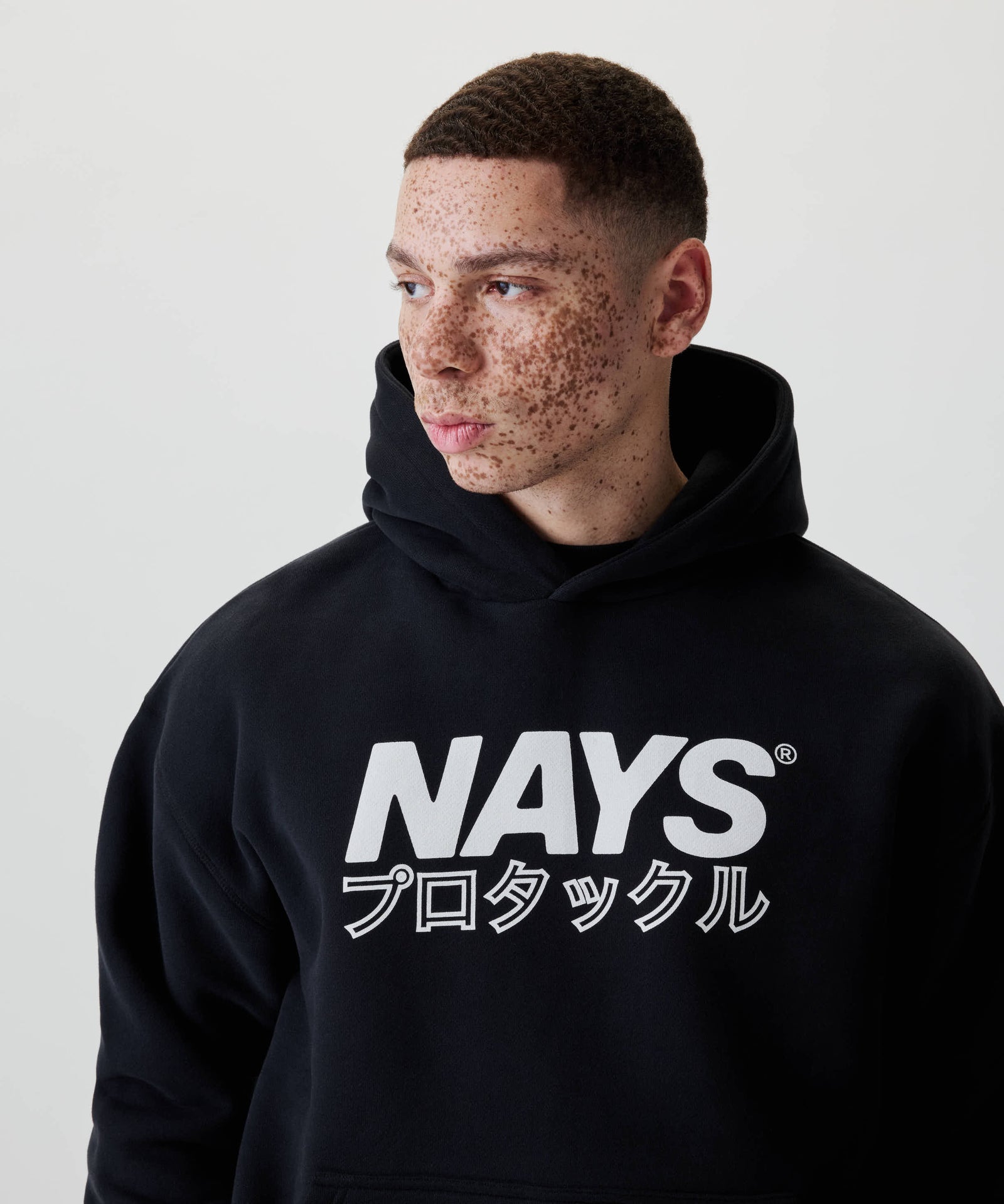 Modell trägt den Nays Understatement Hoodie mit weißem Print NAYS und japanischen Zeichen, im entspannten Oversized Fit, aus 100% Baumwolle für Komfort und Wärme.