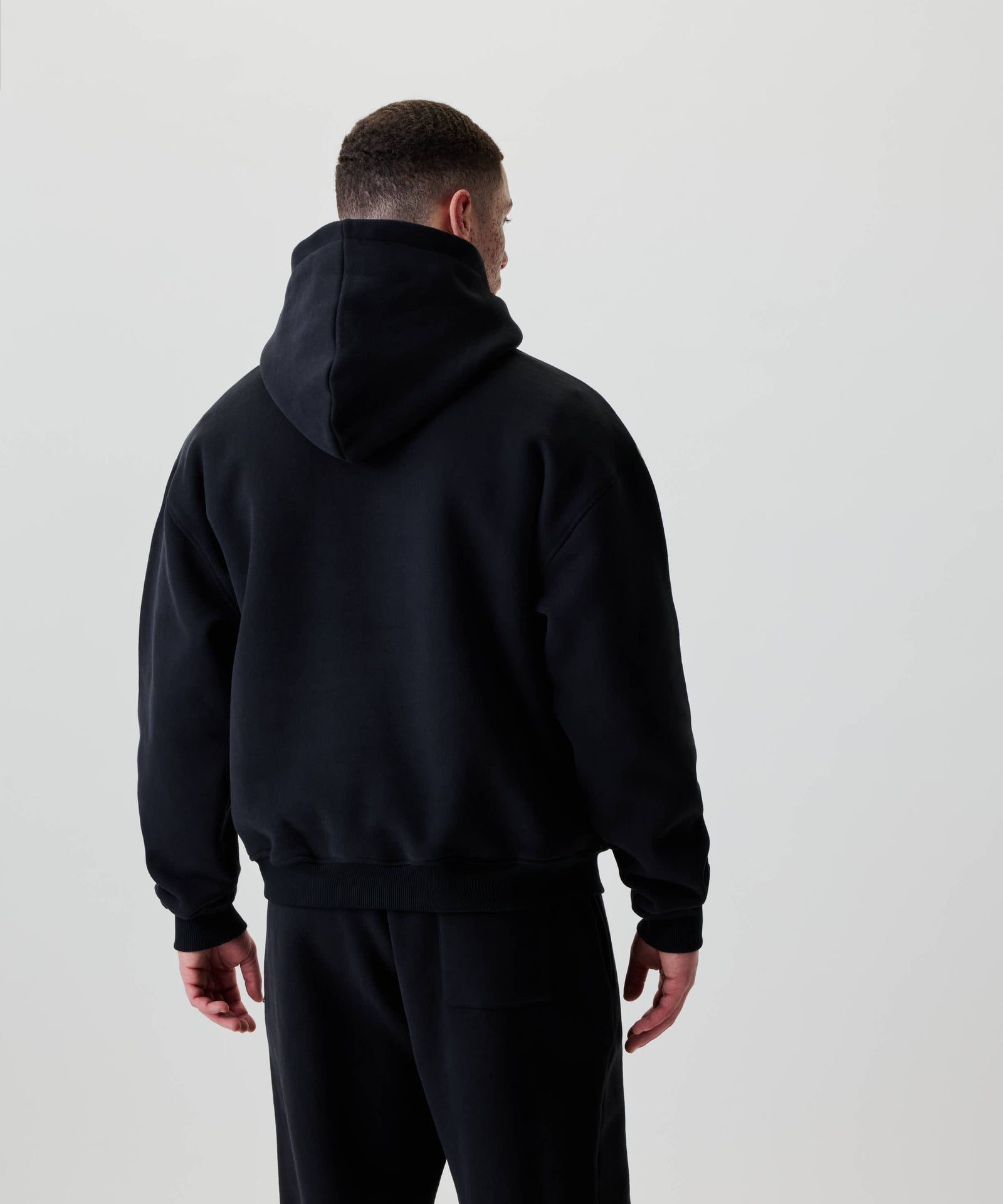 Person von hinten im Nays Understatement Hoodie, schwarz und oversized, mit weißem Frontprint. Aus 100% Baumwolle für Komfort und Wärme, ideal für Alltag und Freizeit.