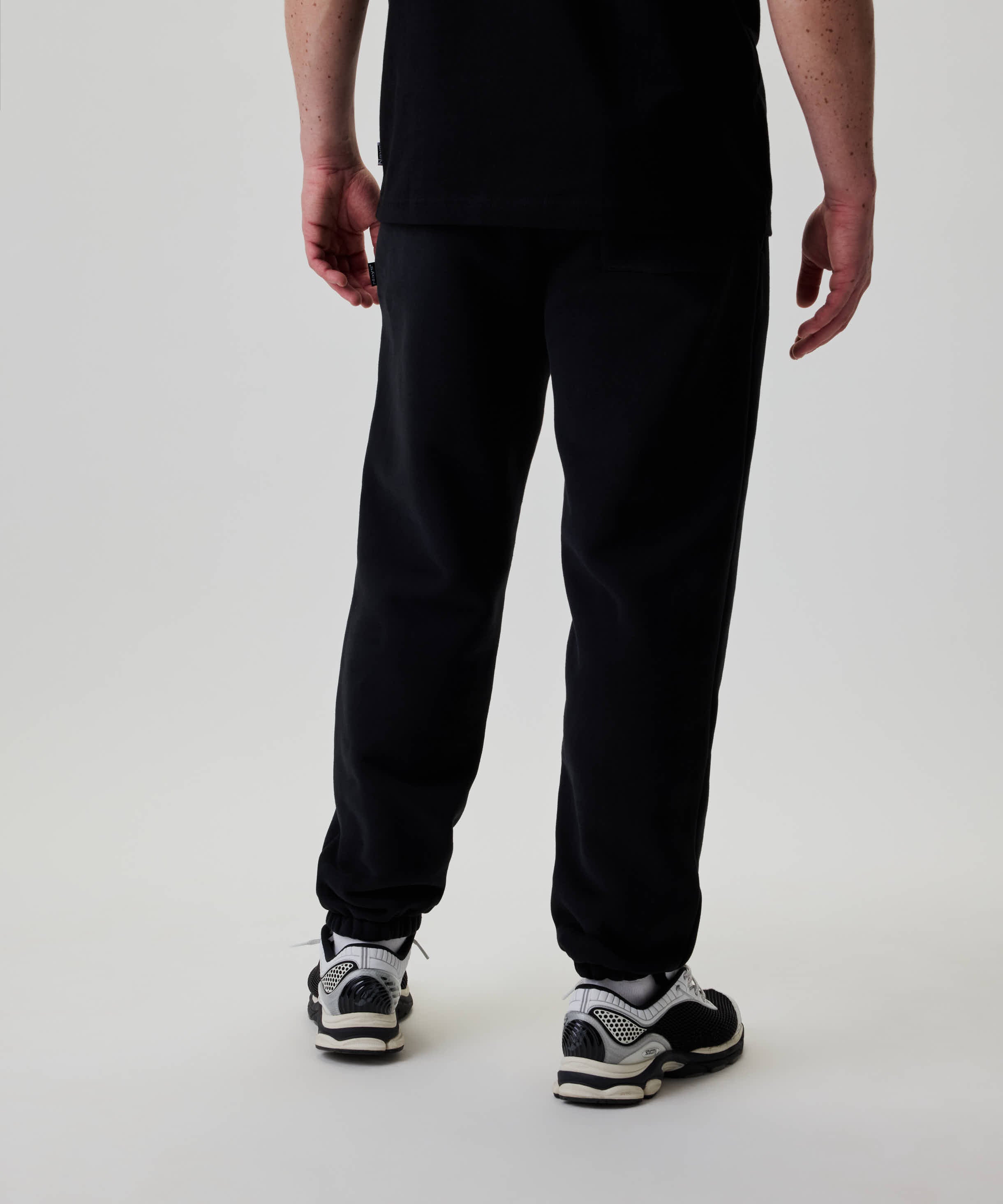 Person trägt Nays Classic Sweatpants mit elastischen Bündchen und Zipper-Taschen, kombiniert mit weißen Socken und schwarz-weißen Sportschuhen, vor neutralem Hintergrund.