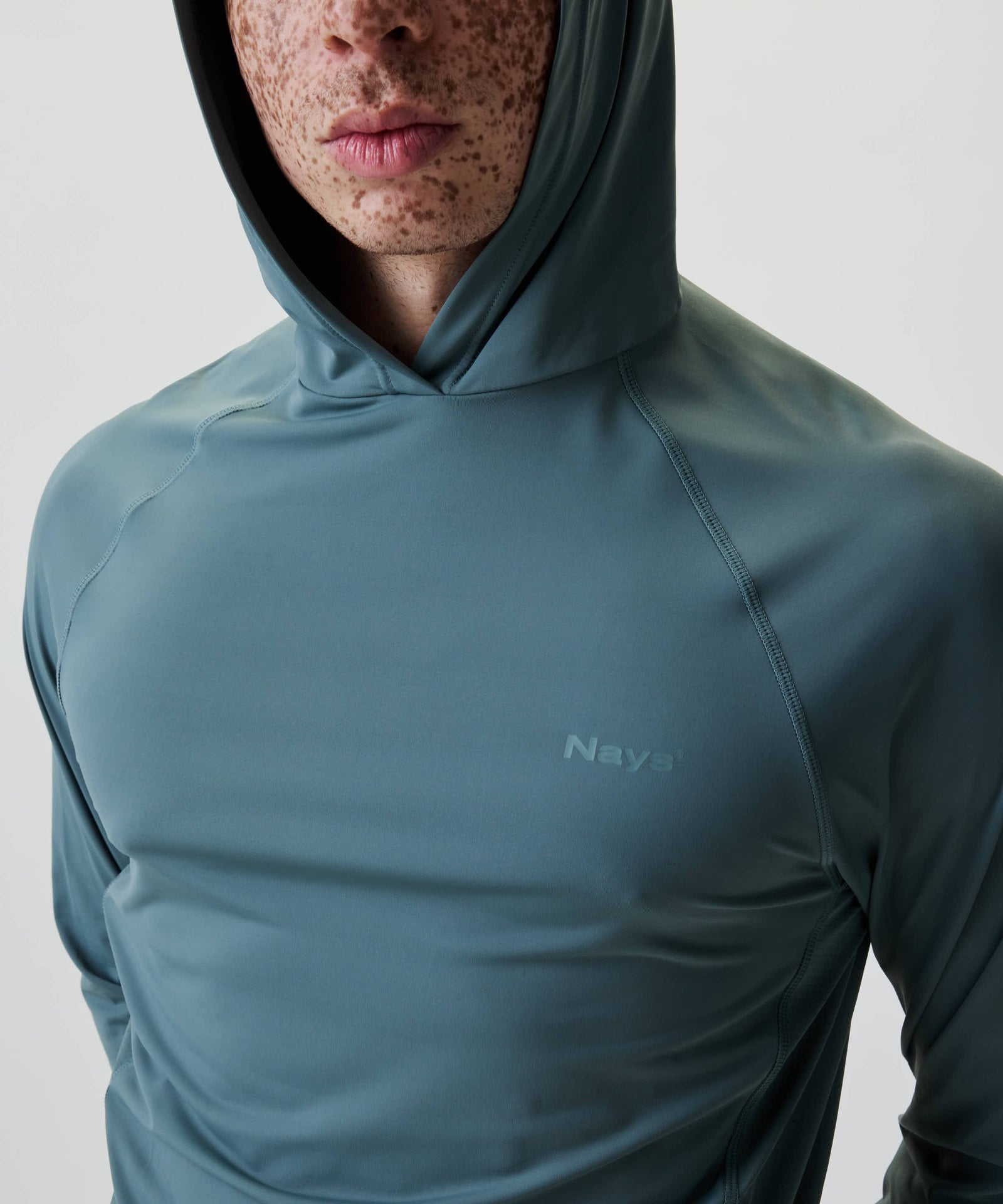 Person trägt das Nays UV 50+ Hooded Longsleeve mit Kapuze und dezentem Logo auf der Brust, ideal für Sonnenschutz bei Outdoor-Aktivitäten.