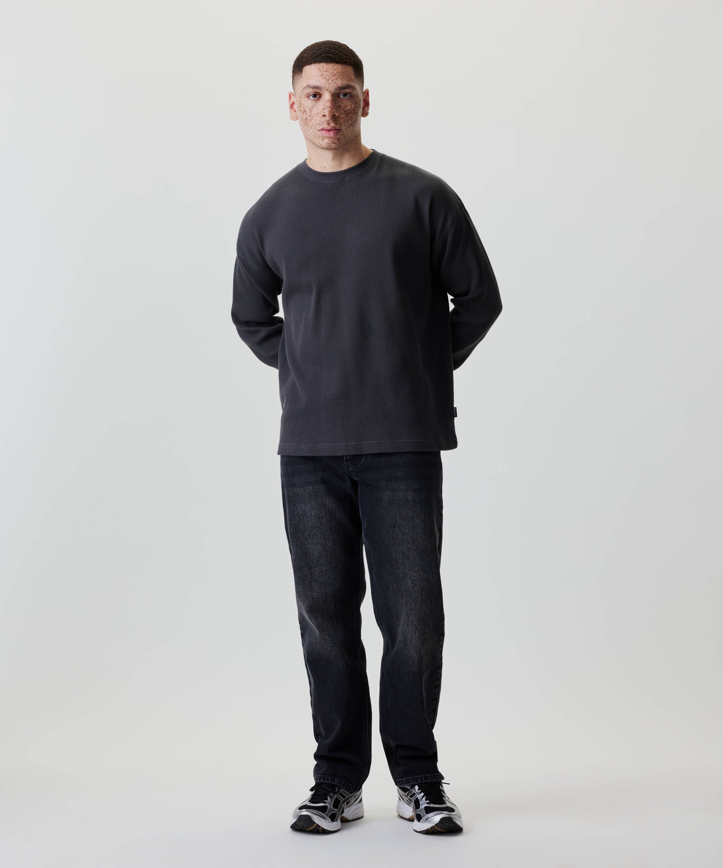 Junger Mann im Nays Classic Waffle Longsleeve, Anthrazit, mit strukturiertem Baumwollmaterial und dezenten Naht-Details, trägt schwarze Jeans und Sneakers.