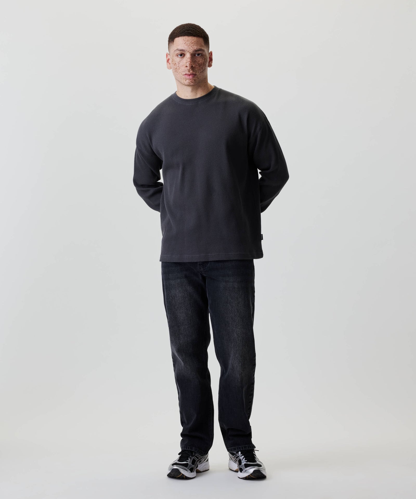 Junger Mann im Nays Classic Waffle Longsleeve, Anthrazit, mit strukturiertem Baumwollmaterial und dezenten Naht-Details, trägt schwarze Jeans und Sneakers.