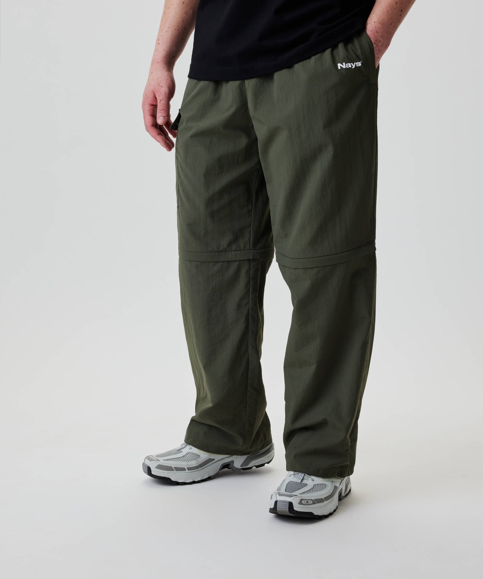 Nays Lightweight Zip Off Pants mit abnehmbaren Beinen und praktischen Reißverschlusstaschen, getragen mit Trailrunning-Sneakern, ideal für flexible Outdoor-Aktivitäten.