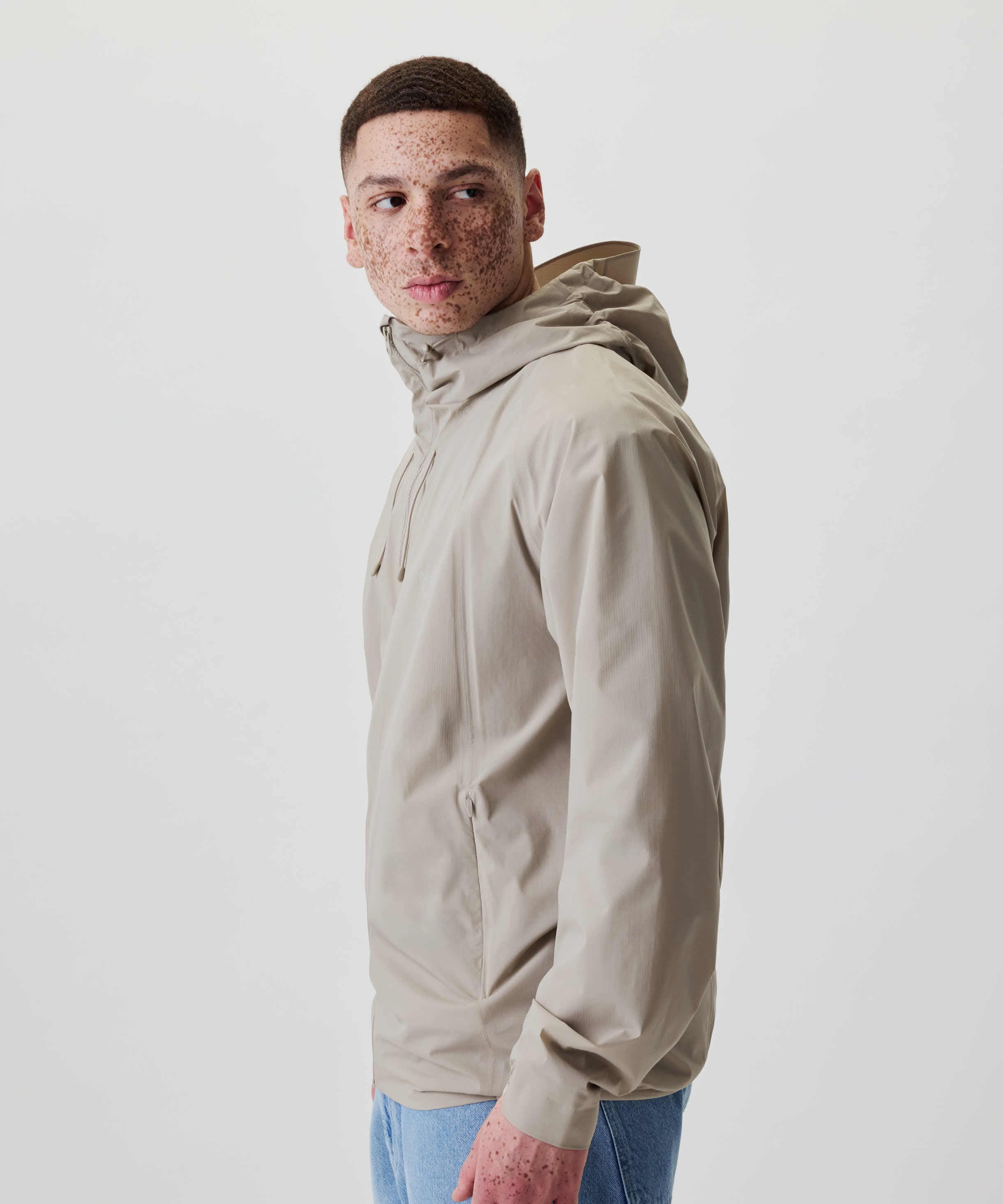 Ein junger Mann trägt die Nays 2L Defend Mono Jacket mit verstellbarer Kapuze und seitlichen Reißverschlusstaschen, ideal für vielseitige Outdoor-Aktivitäten.