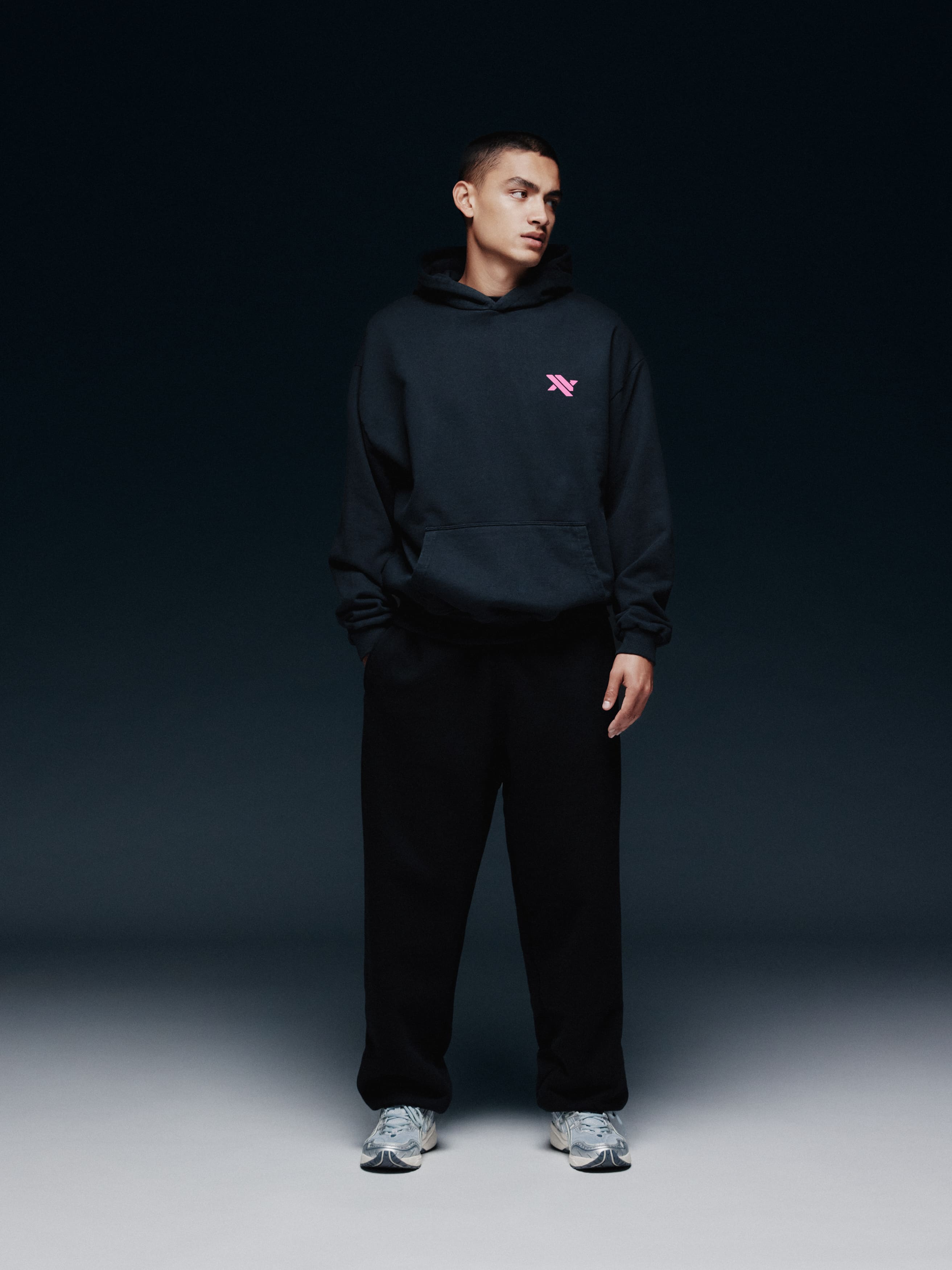 Model trägt den schwarzen NAYS TRN Hoodie in Frontansicht mit rosa Logo.