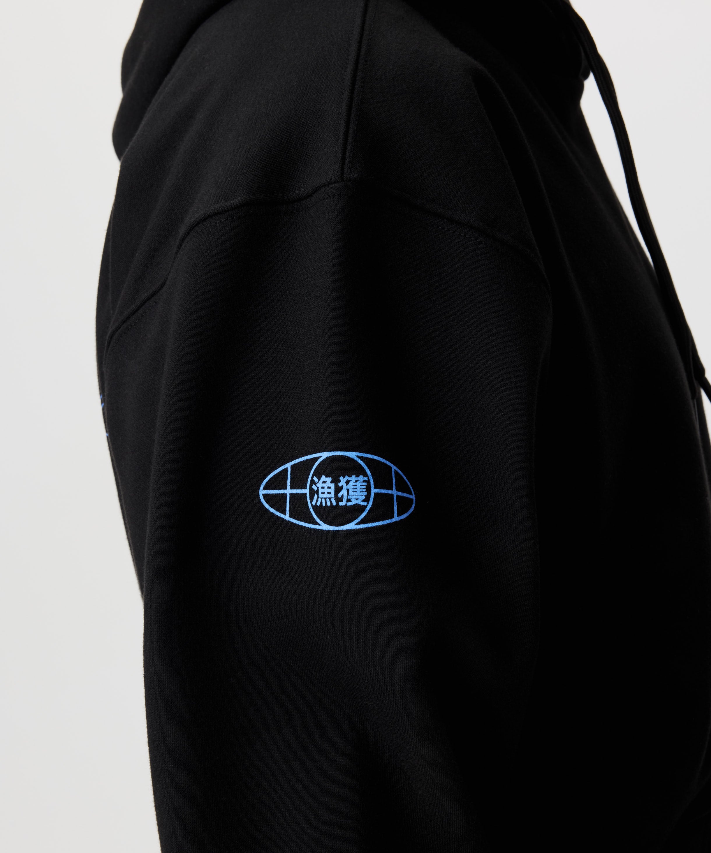 Detailansicht, Mann im Seitenprofil im schwarzen Kapuzen-Pullover. Fokus auf blauen Aermel-Print, der an einen Globus erinnert.