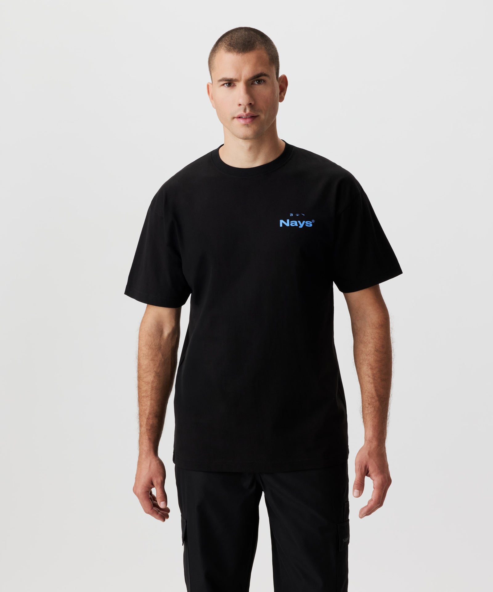 Vorderansicht Mann im schwarzen T-Shirt und schwarzer Hose. Das T-Shirt hat einen blauen Print auf der Brust.