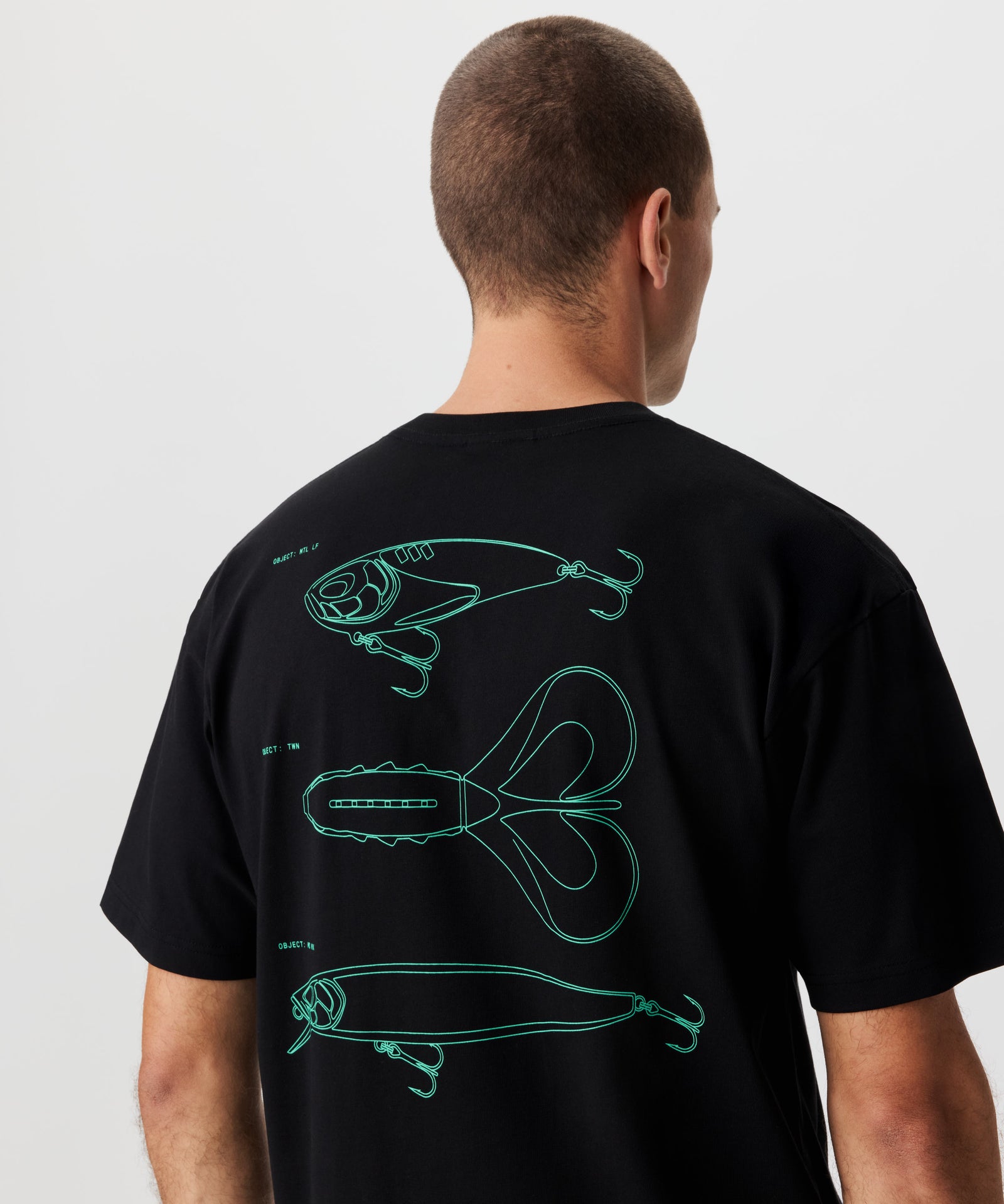 Rückansicht Mann im schwarzen T-Shirt und grünem Rücken-Print. Der Print zeige drei bekannte Köder-Silhouetten.