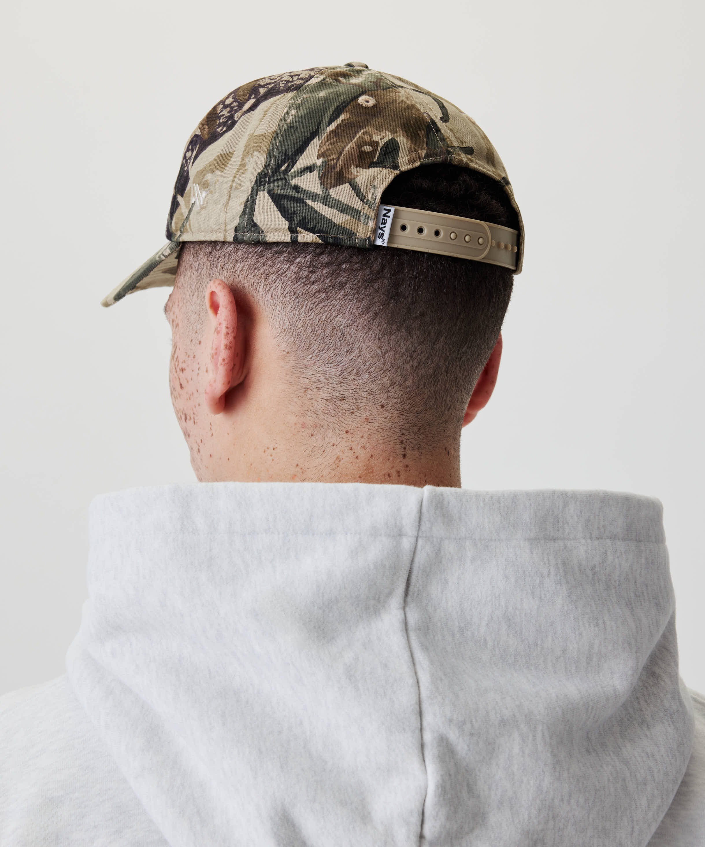 Person mit Nays Fishing Club Cap in Camouflage-Print, rückwärts getragen, zeigt den verstellbaren Snapback-Verschluss für eine individuelle Passform und Komfort.