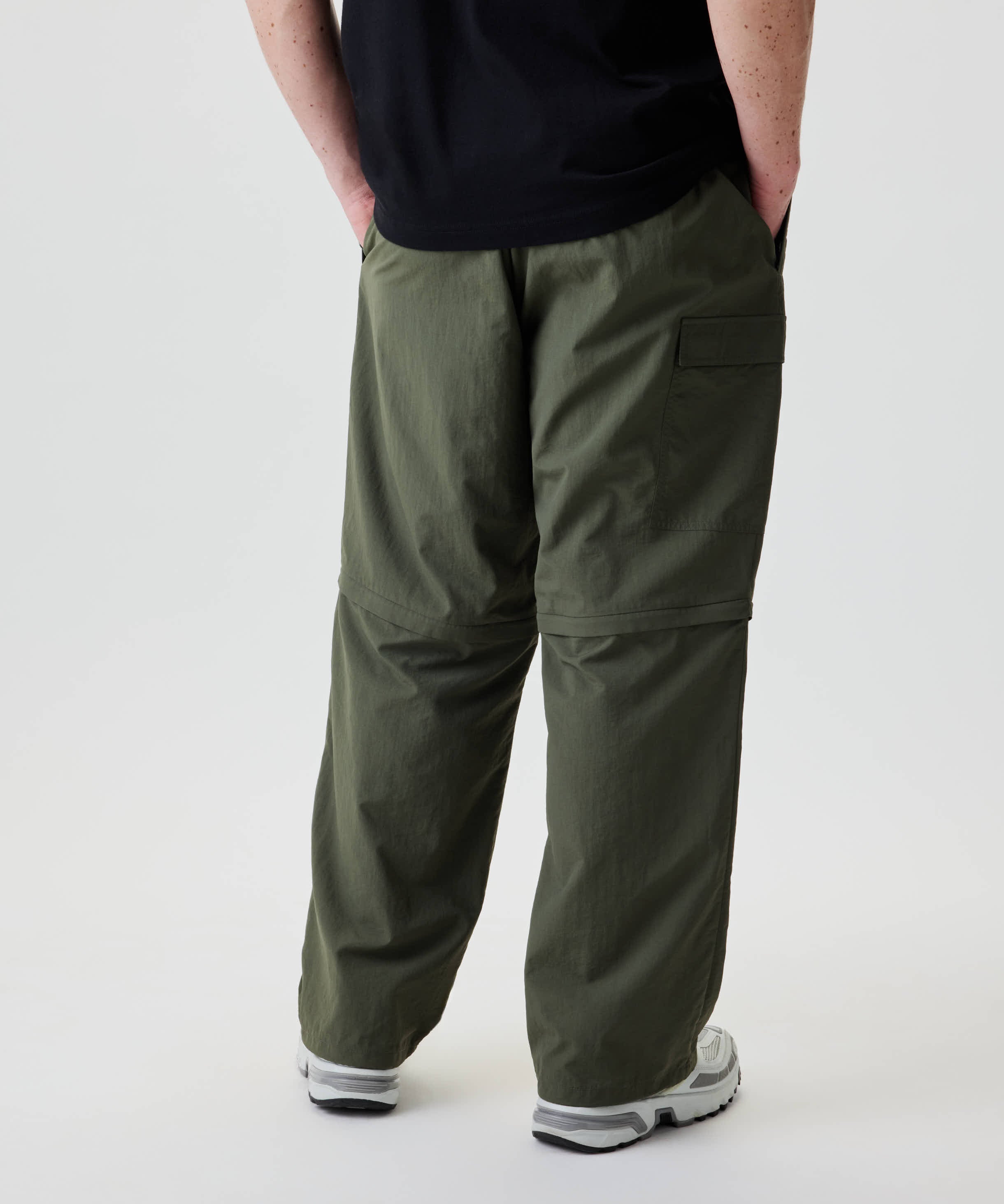 Nays Lightweight Zip Off Pants mit seitlicher Klappentasche und Reißverschluss, getragen mit weißen Trail-Sneakern. Ideal für variable Bedingungen durch abnehmbare Hosenbeine.