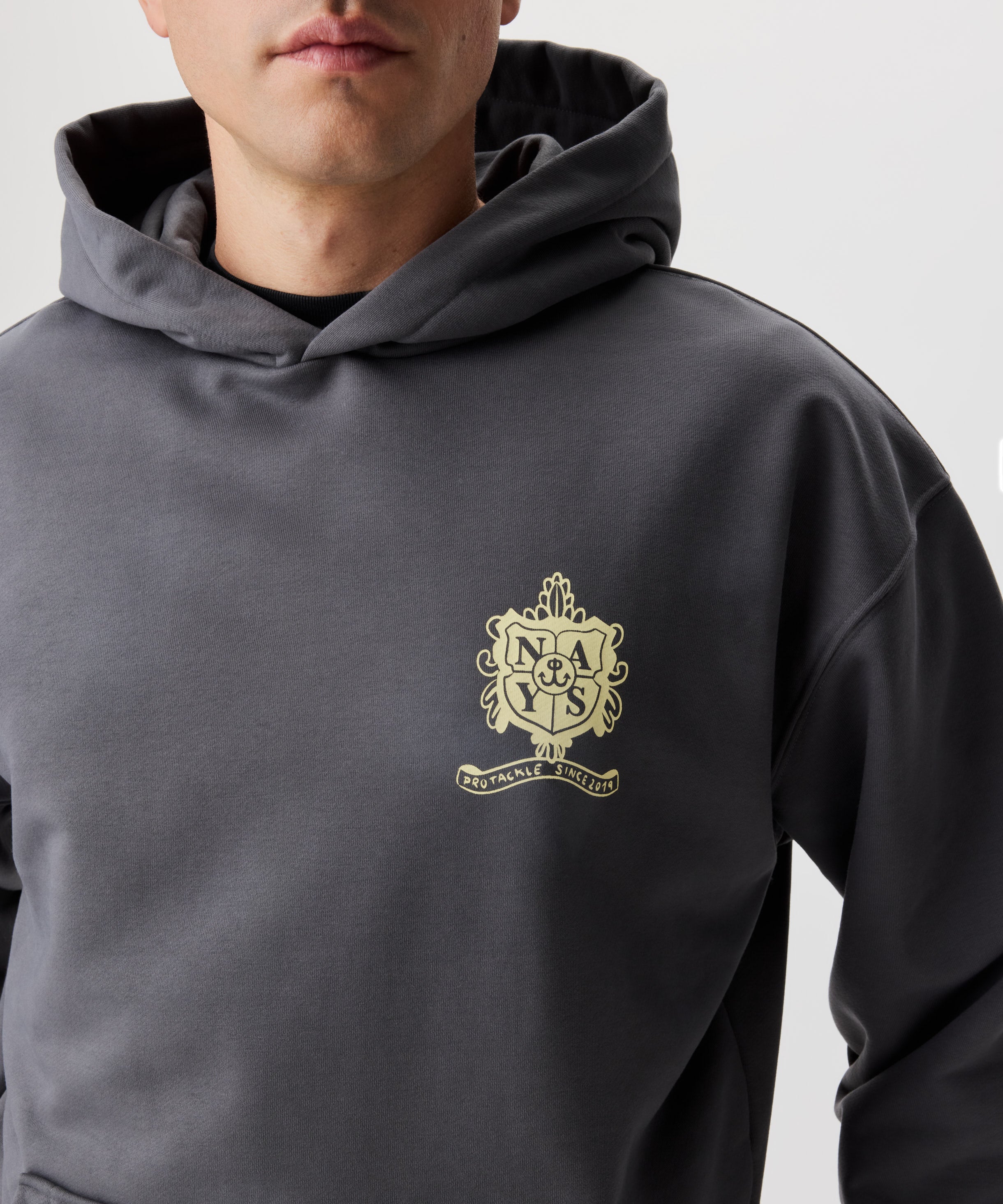 Frontansicht Mann im grauen Kapuzen Sweatshirt. Das Sweatshirt hat einen gelben Druck auf der linken Brust.