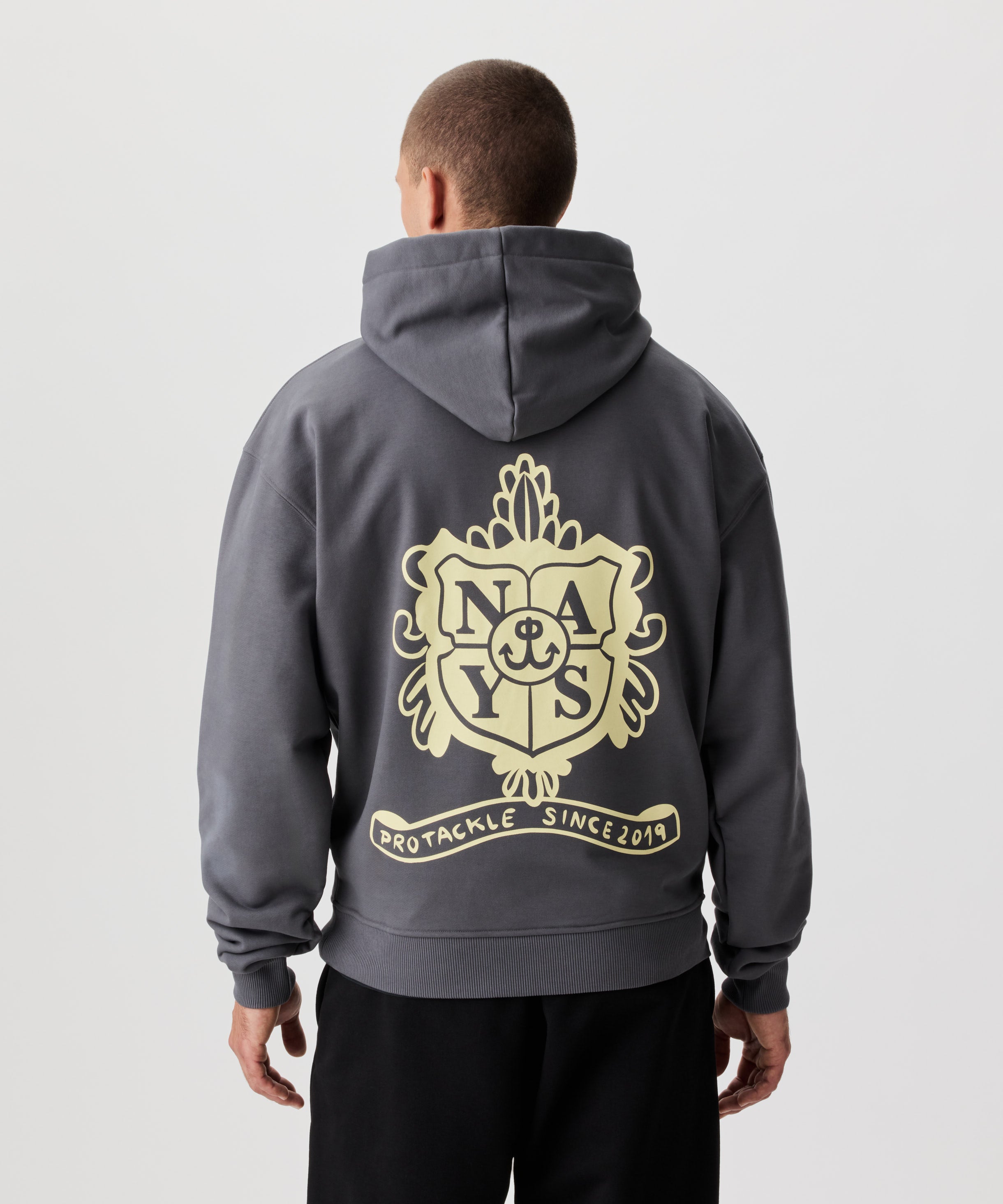 Rückansicht Mann im grauen Kapuzen Sweatshirt und schwarzer Hose. Das Sweatshirt verfügt über einen großen, gelben Aufdruck auf dem Rücken.