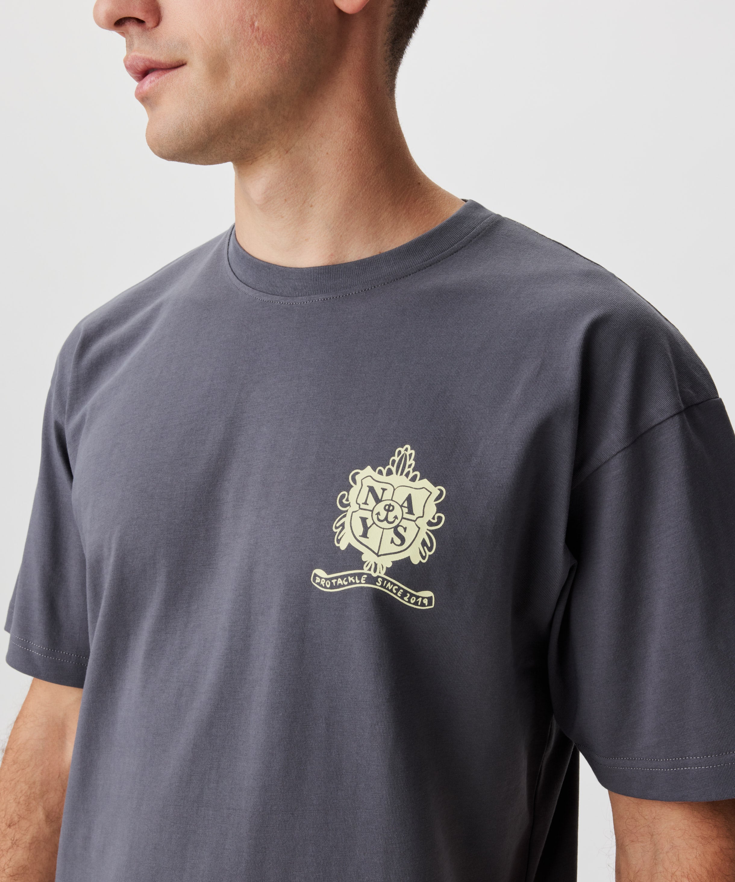 Frontansicht Mann im grauen T-Shirt. Das T-Shirt hat einen gelben Druck auf der linken Brust.