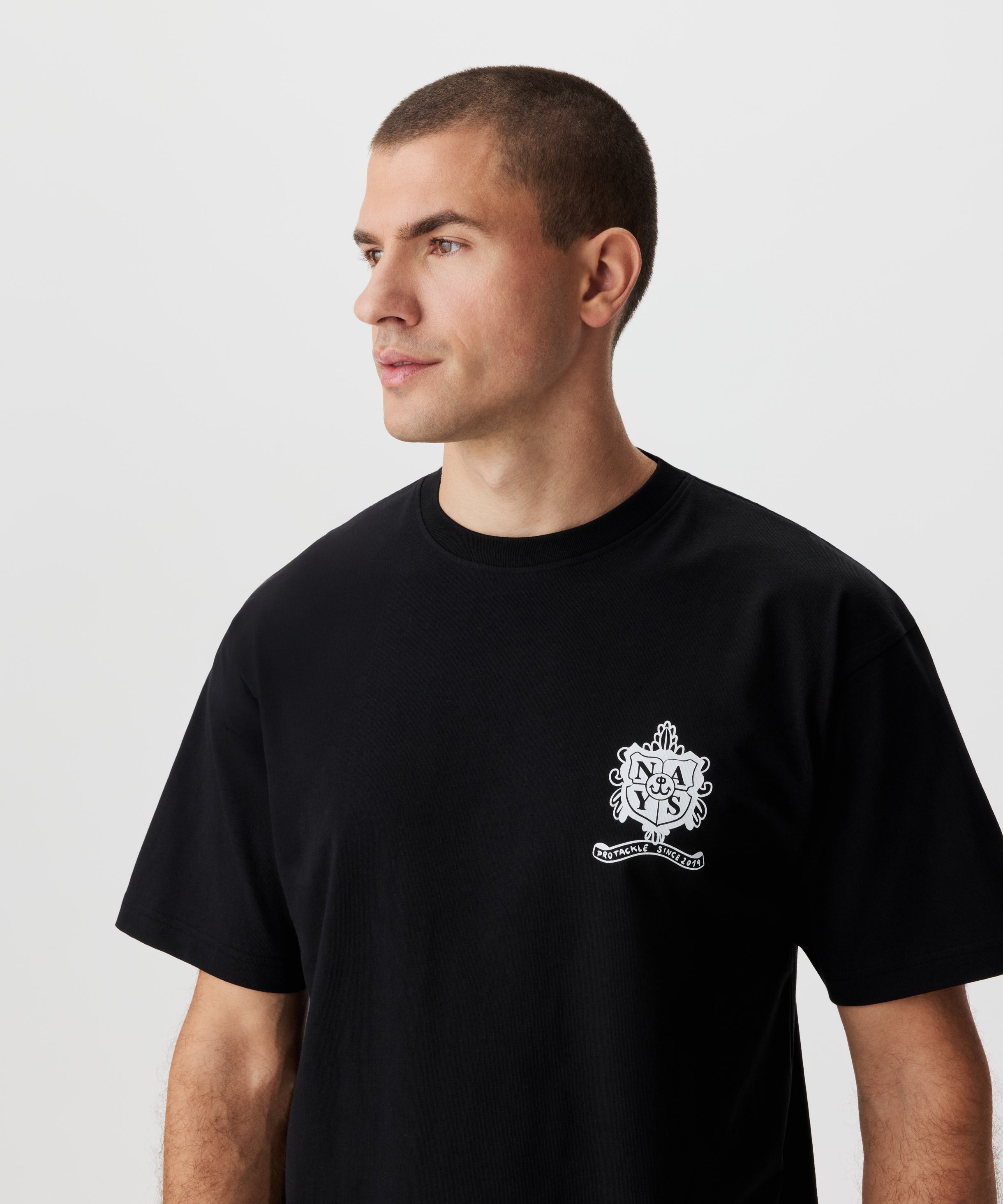 Frontansicht Mann im schwarzen T-Shirt. Das T-Shirt hat einen weißen Druck auf der linken Brust.