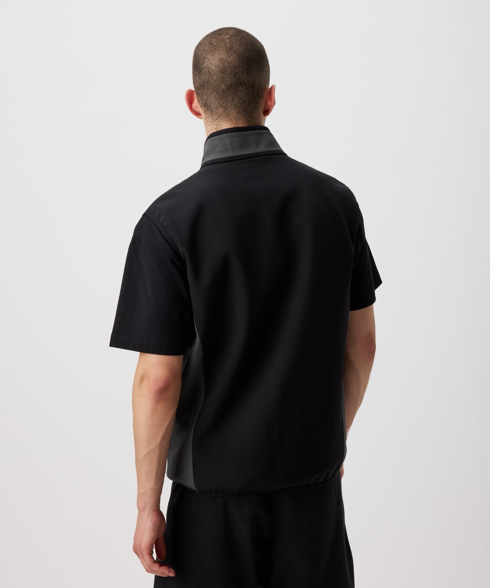Ein Mann von hinten zu sehen trägt eine dünne, funktionelle Weste in schwarz. Die Seiten und der Kragen sind farblich in grau abgesetzt.