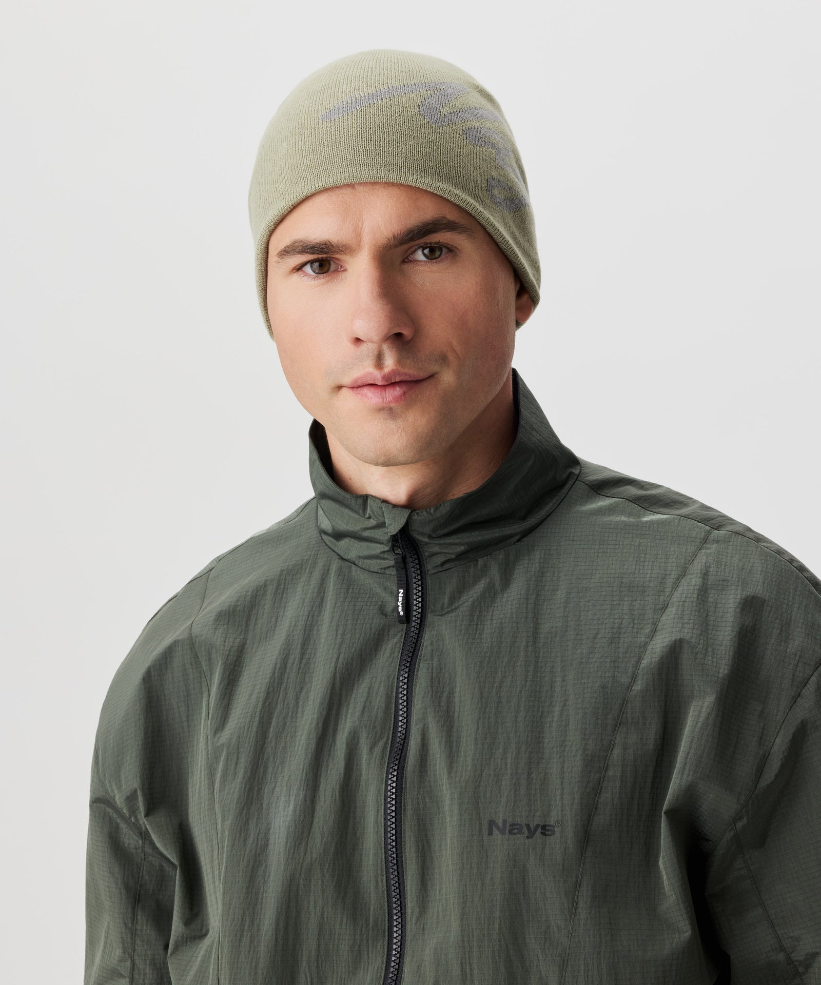 Frontansicht Mann in grüner Jacke und grüner Strickmütze mit grauen Nays-Logo-Schriftzug.