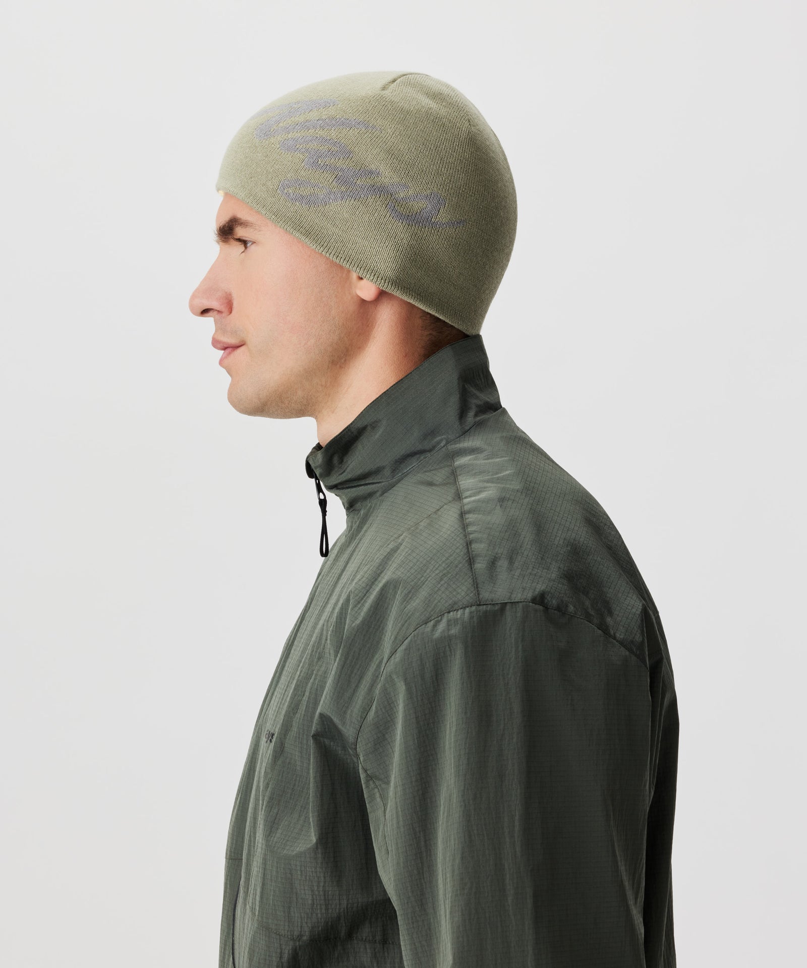 Seitliche Ansicht Mann in grüner Jacke und grüner Strickmütze mit grauem Nays-Logo-Schriftzug.