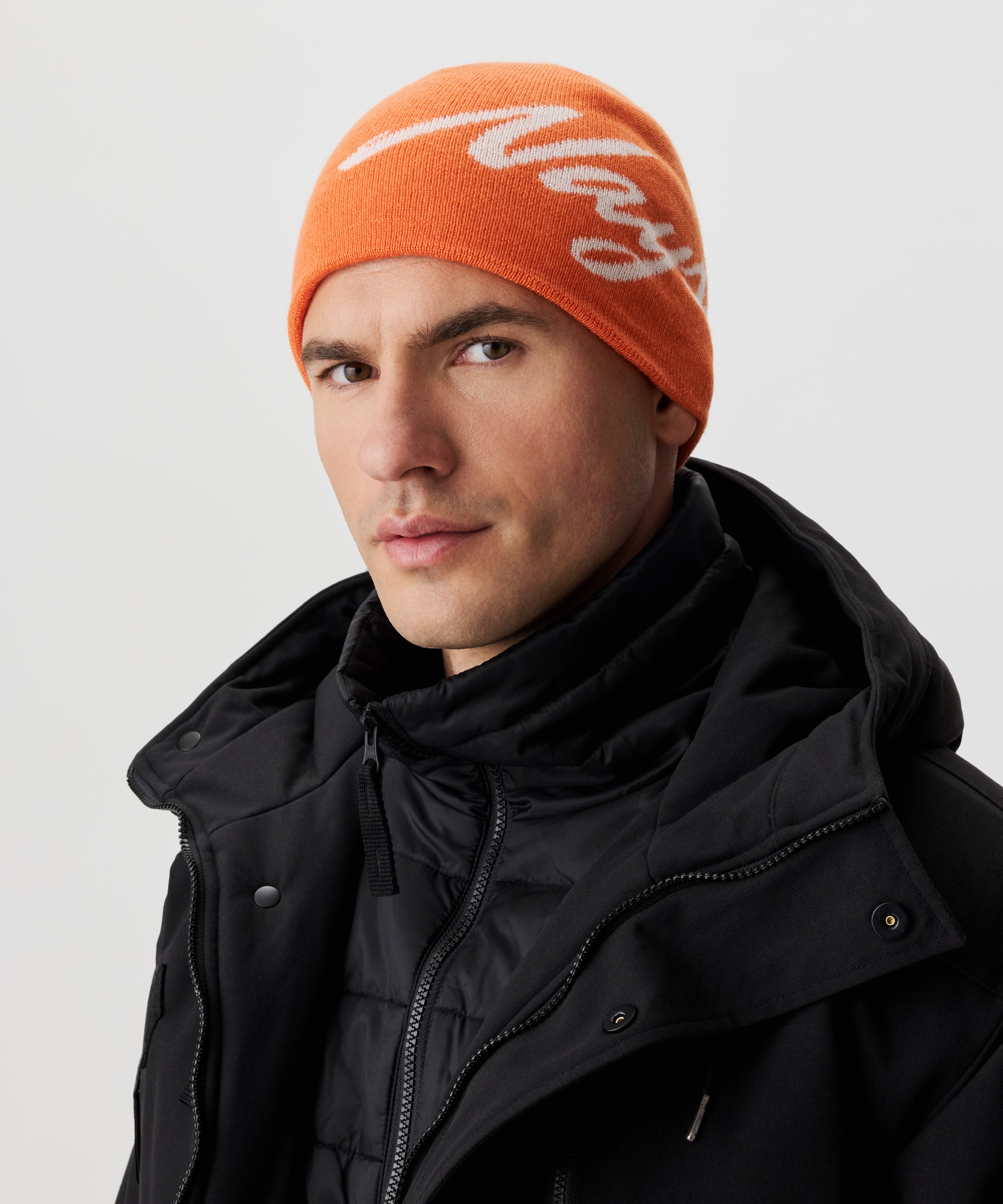 Frontansicht Mann  in schwarzer Jacke und orange-farbiger Strickmütze mit weißem Nays-Logo-Schriftzug.