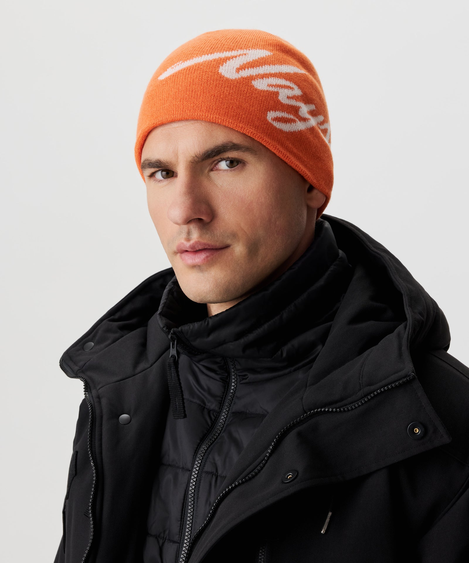 Frontansicht Mann  in schwarzer Jacke und orange-farbiger Strickmütze mit weißem Nays-Logo-Schriftzug.