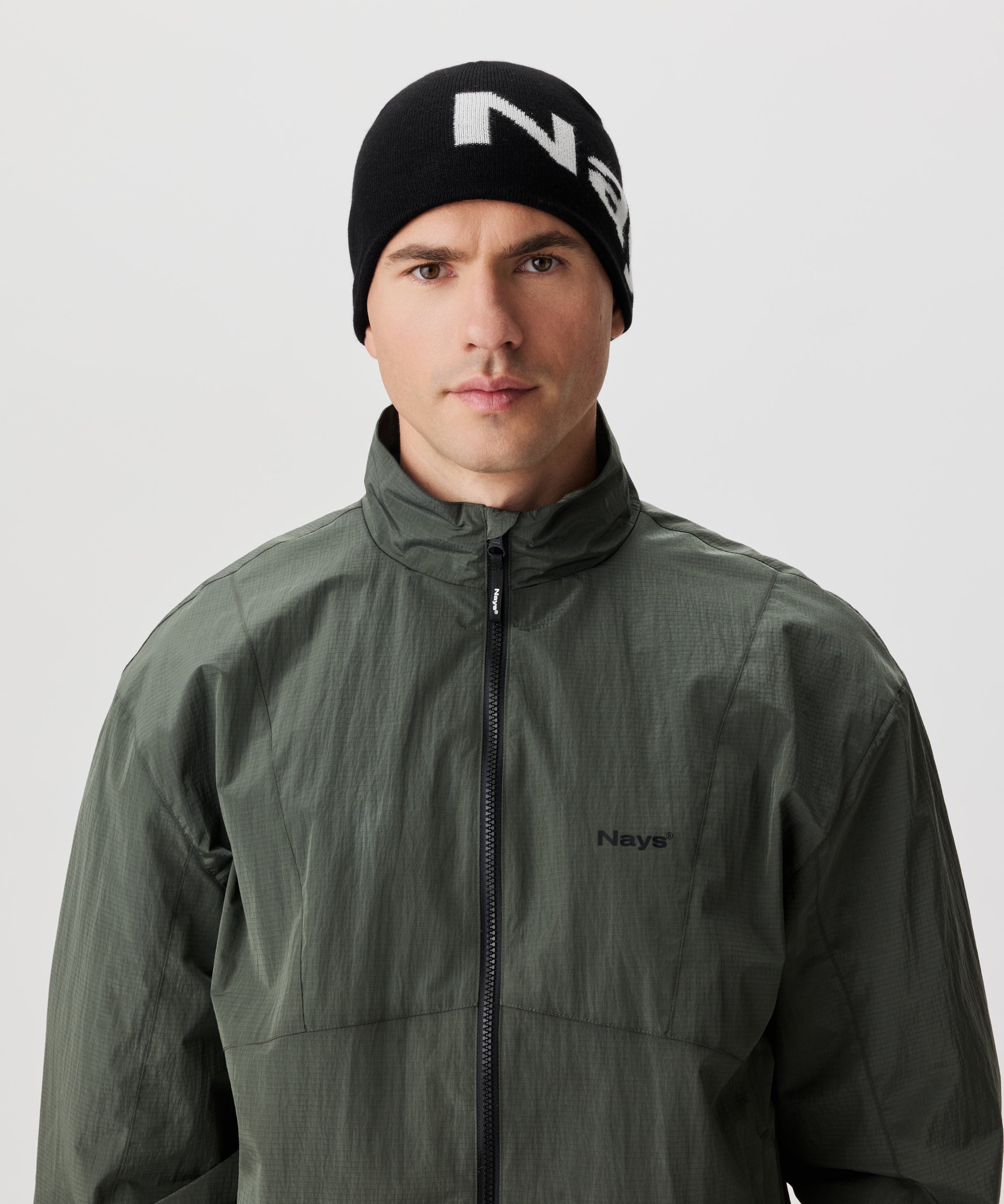 Frontale Ansicht Mann in grüner Jacke und schwarzer Strickmütze mit weißem Nays-Logo-Schriftzug.