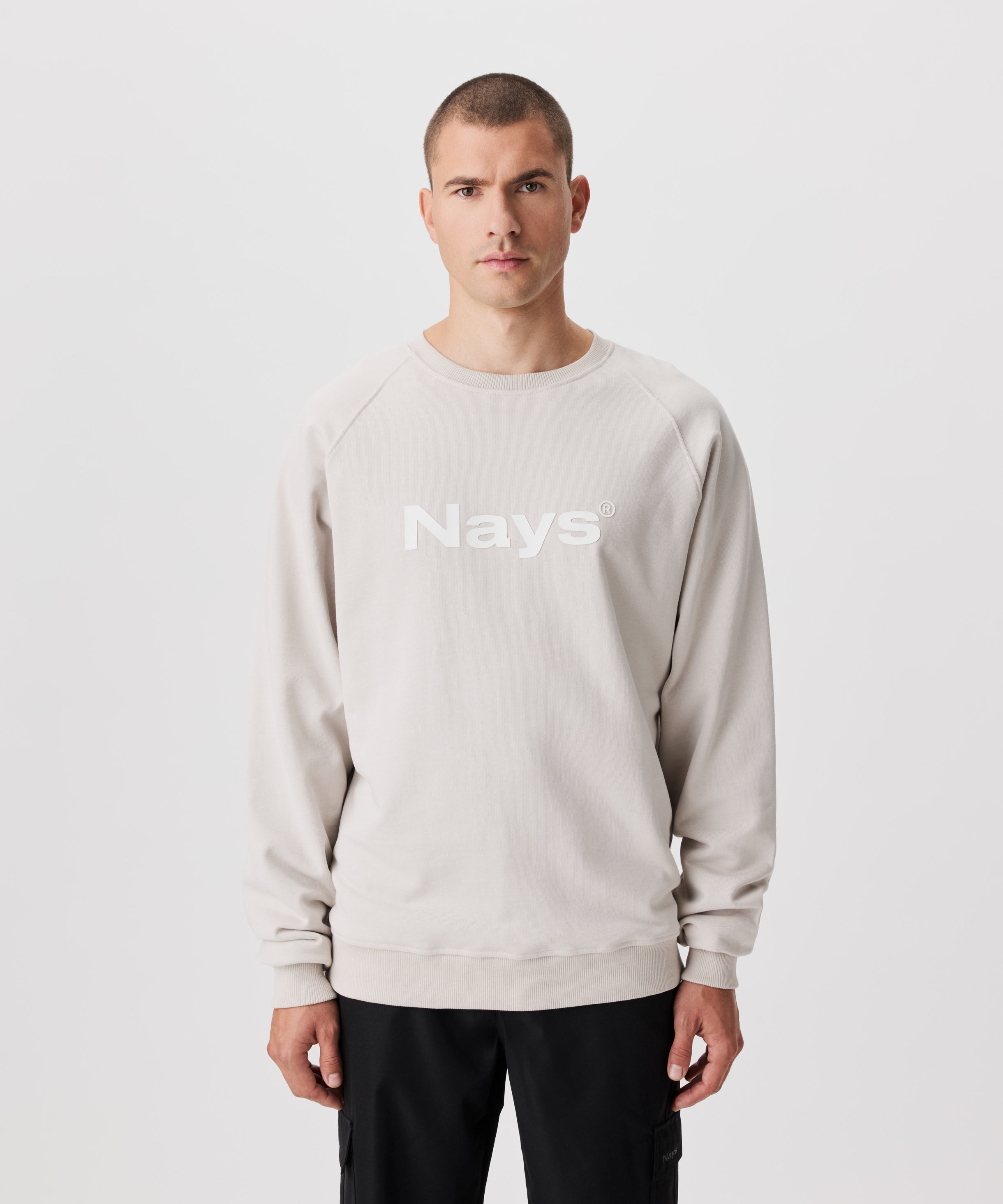 Frontansicht Mann mit mit beigefarbenem Pullover und weißem Nays-Logo-Druck auf der Brust.