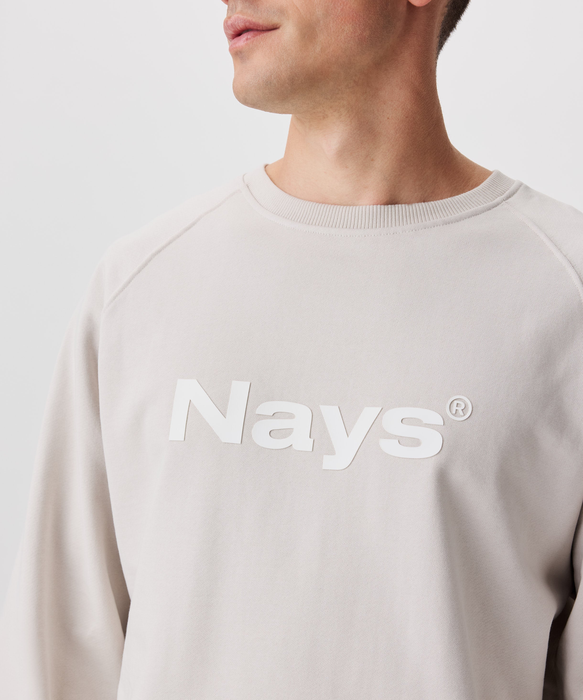 Frontale Ansicht Mann mit mit beigefarbenem Pullover und weißem Nays-Logo-Druck auf der Brust.