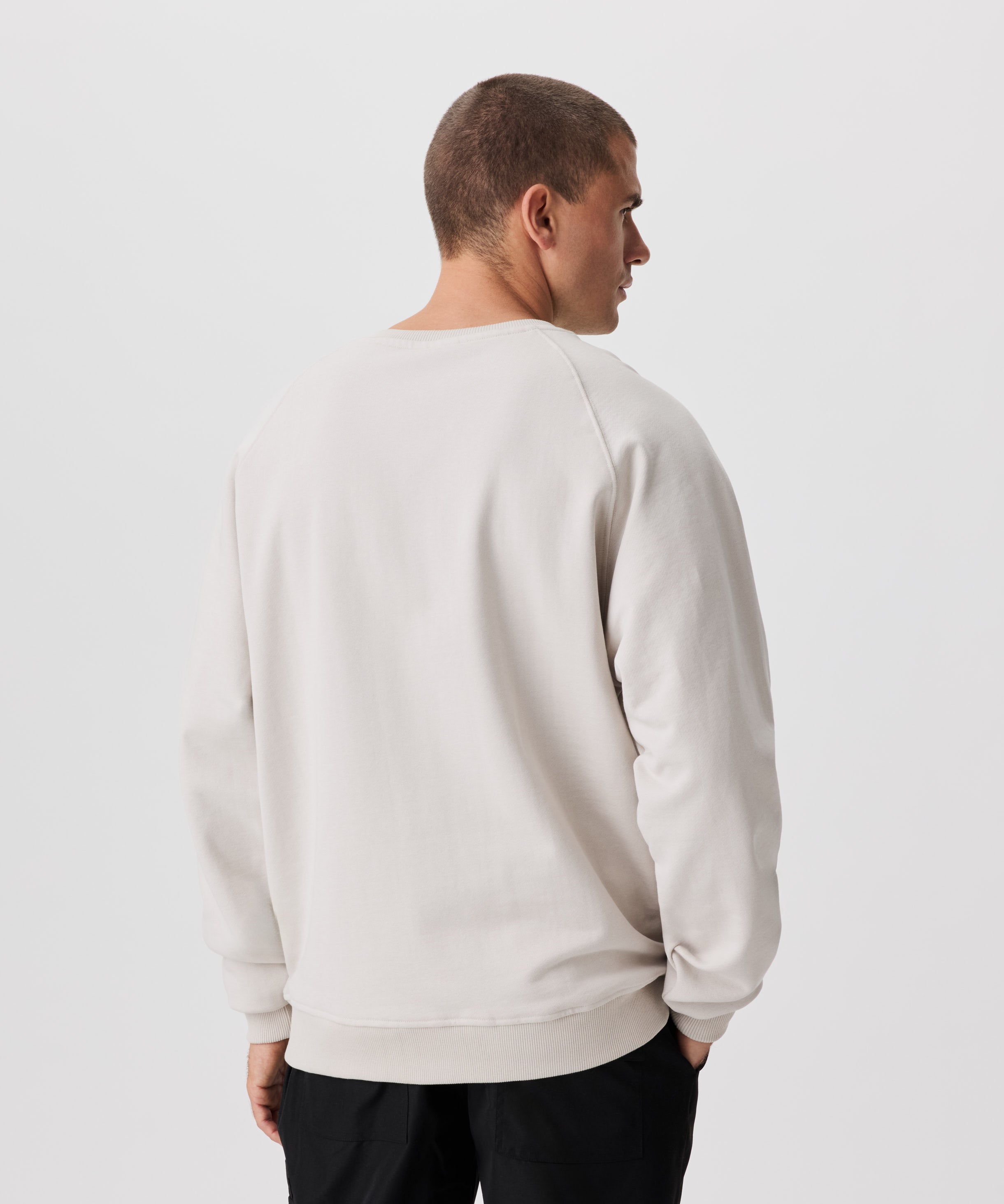 Rückansicht Mann mit mit beigefarbenem Pullover und schwarzer Hose.