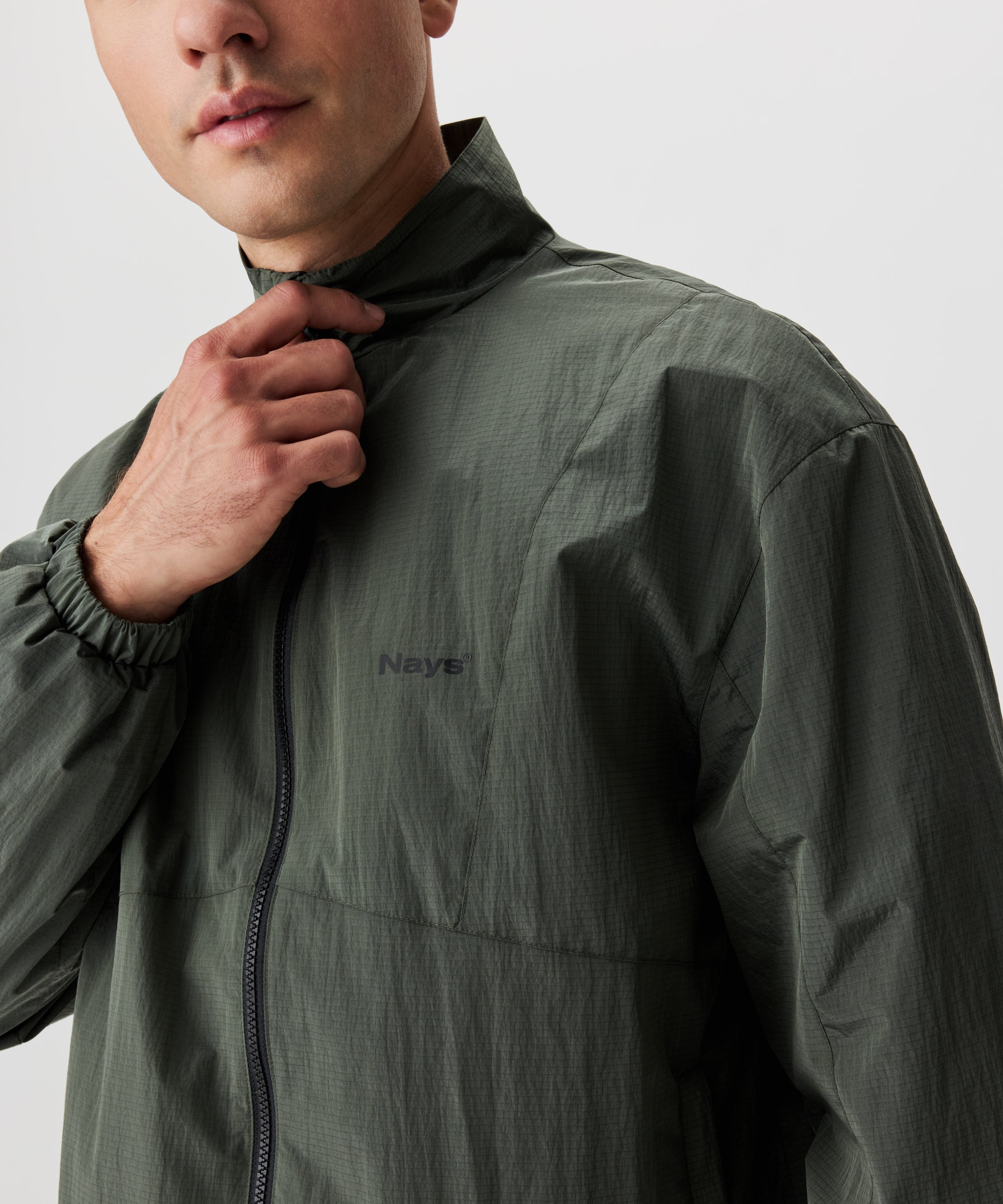 Mann in grüner Blouson Jacke. Die Jacke hat einen schwarzen Reißverschluss und eine kleines Nays-Logo auf der linken Brust.