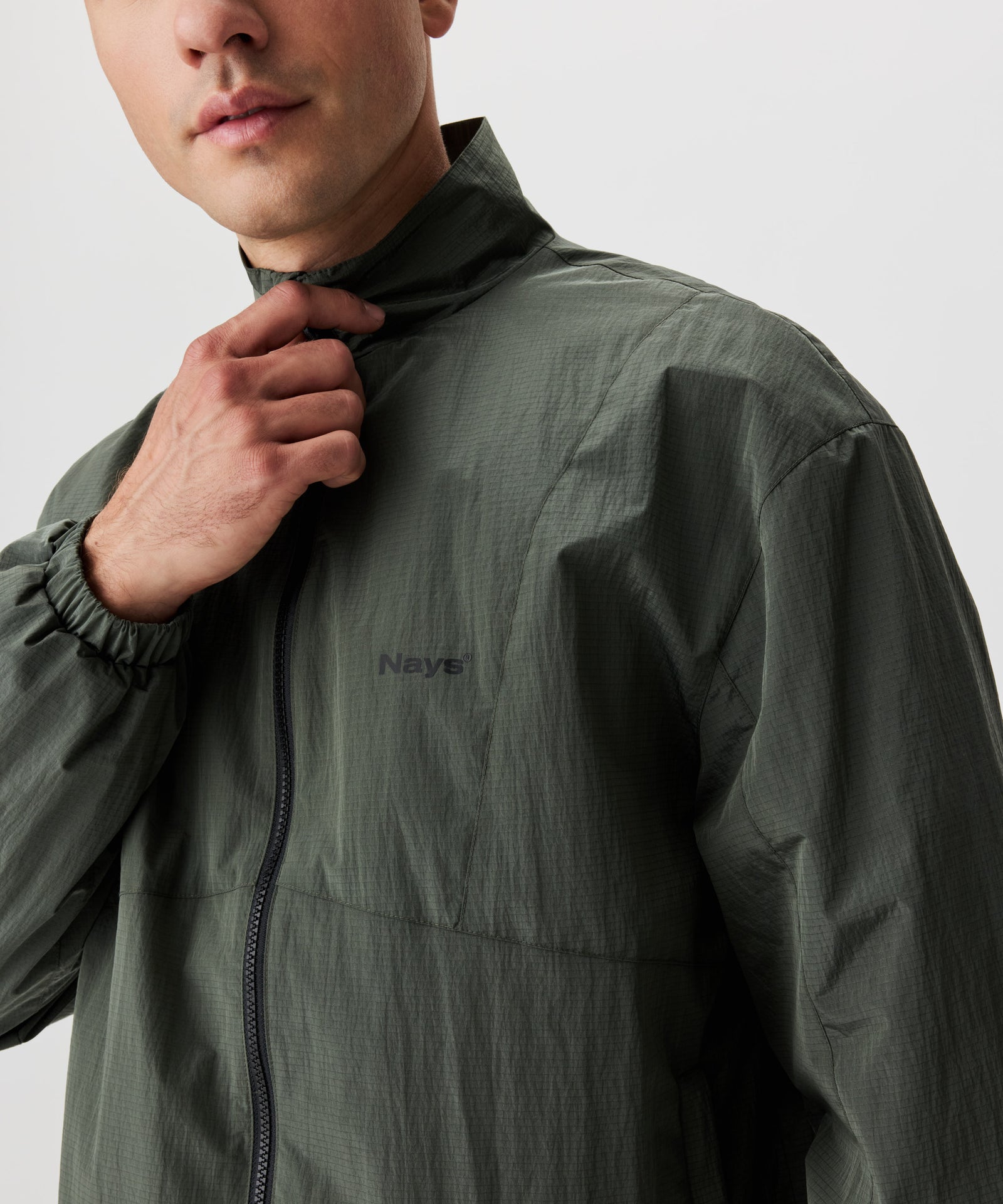 Mann in grüner Blouson Jacke. Die Jacke hat einen schwarzen Reißverschluss und eine kleines Nays-Logo auf der linken Brust.