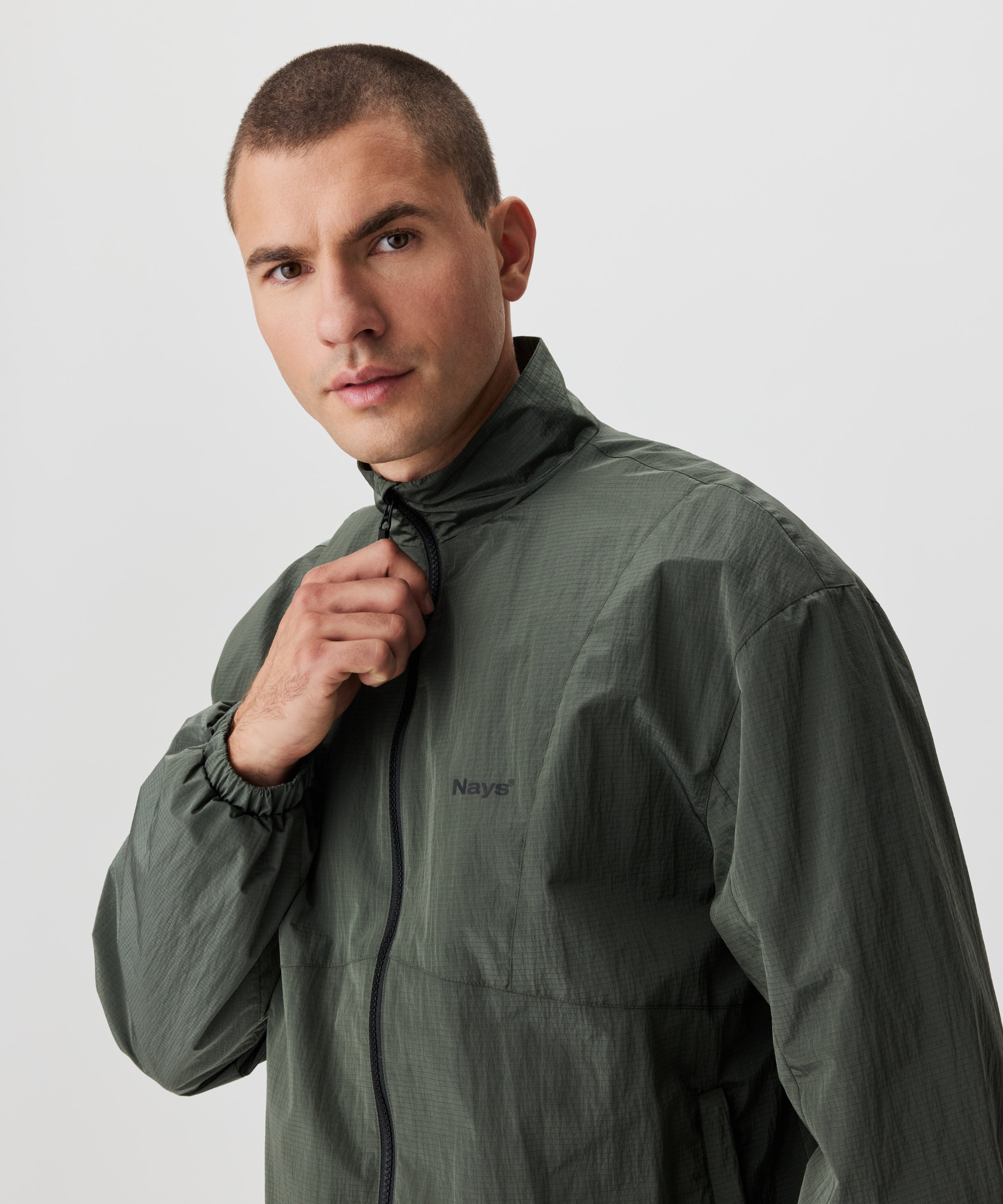 Mann in grüner Blouson Jacke. Die Jacke hat einen schwarzen Reißverschluss und eine kleines Nays-Logo auf der linken Brust.