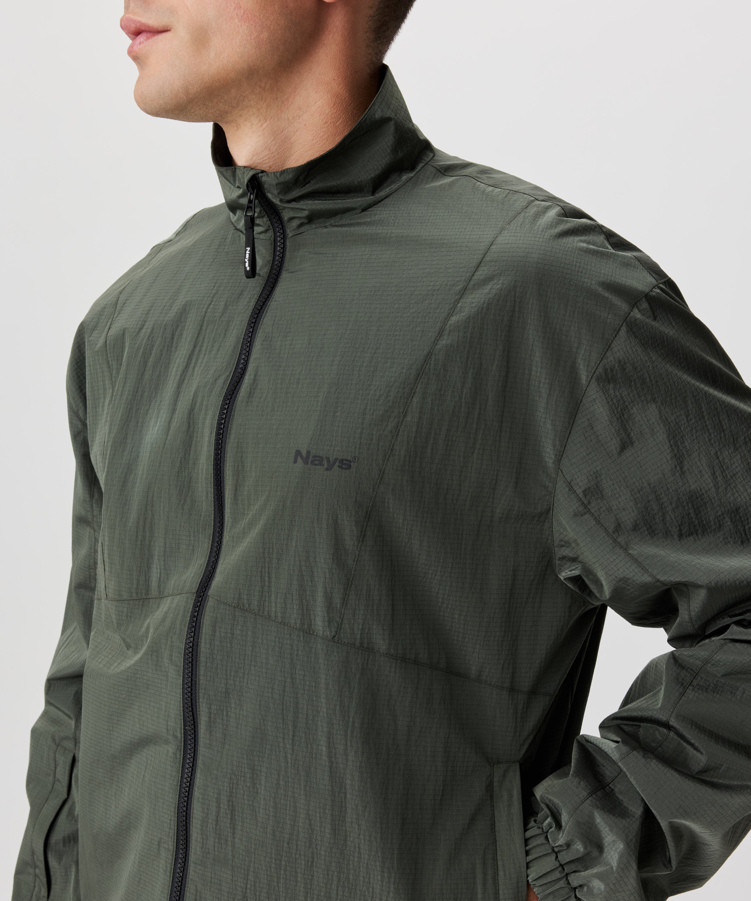 Mann in grüner Blouson Jacke in der seitlichen Frontansicht. Die Jacke hat einen schwarzen Reißverschluss und eine kleines Nays-Logo auf der linken Brust.