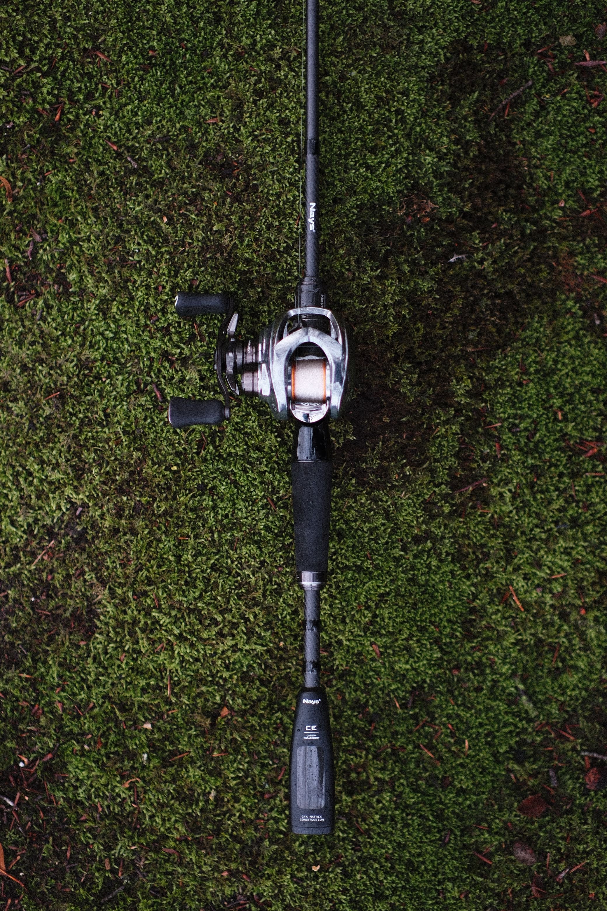 Nays Baitcast Raubfisch Angelrute auf grünem Moos liegend.