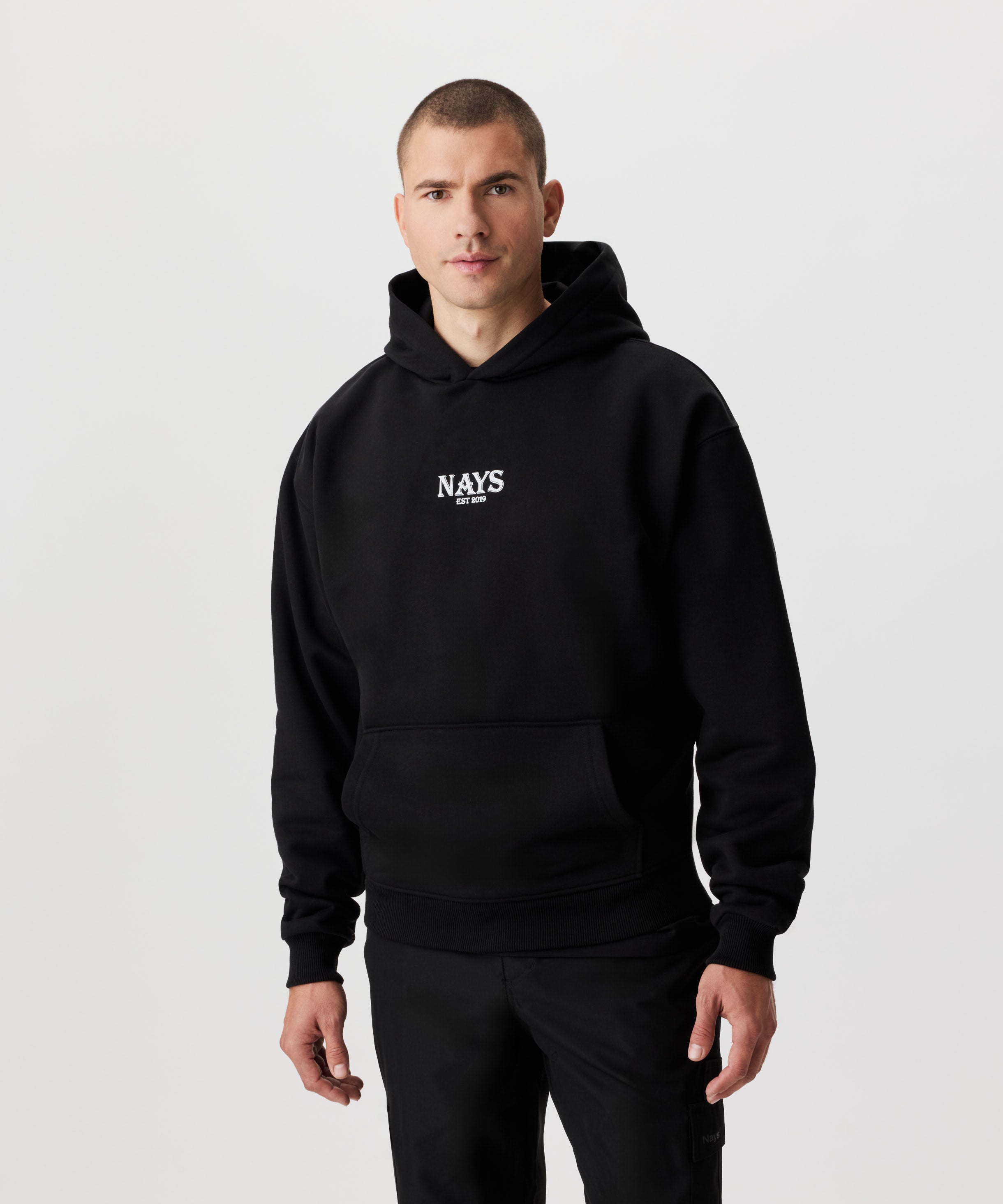 Mann im schwarzen Kapuzen Sweatshirt in der Frontansicht. Das Sweatshirt hat einen mittig gesetztes Nays-Logo in weiß.