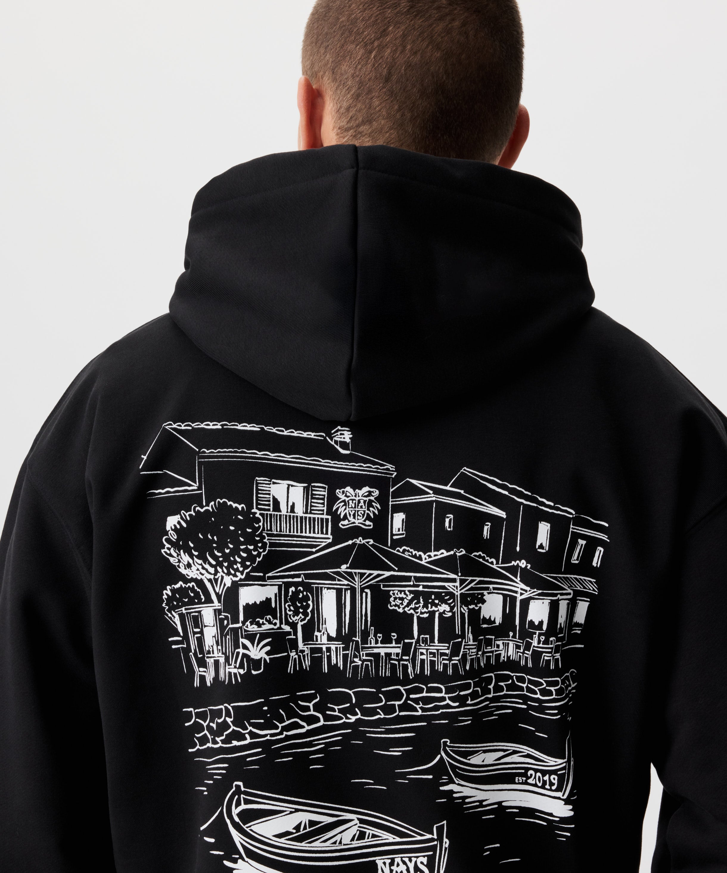 Rückansicht Mann im schwarzen Kapuzen Sweatshirt. Das Sweatshirt hat einen auffälligen Druck in weiß.