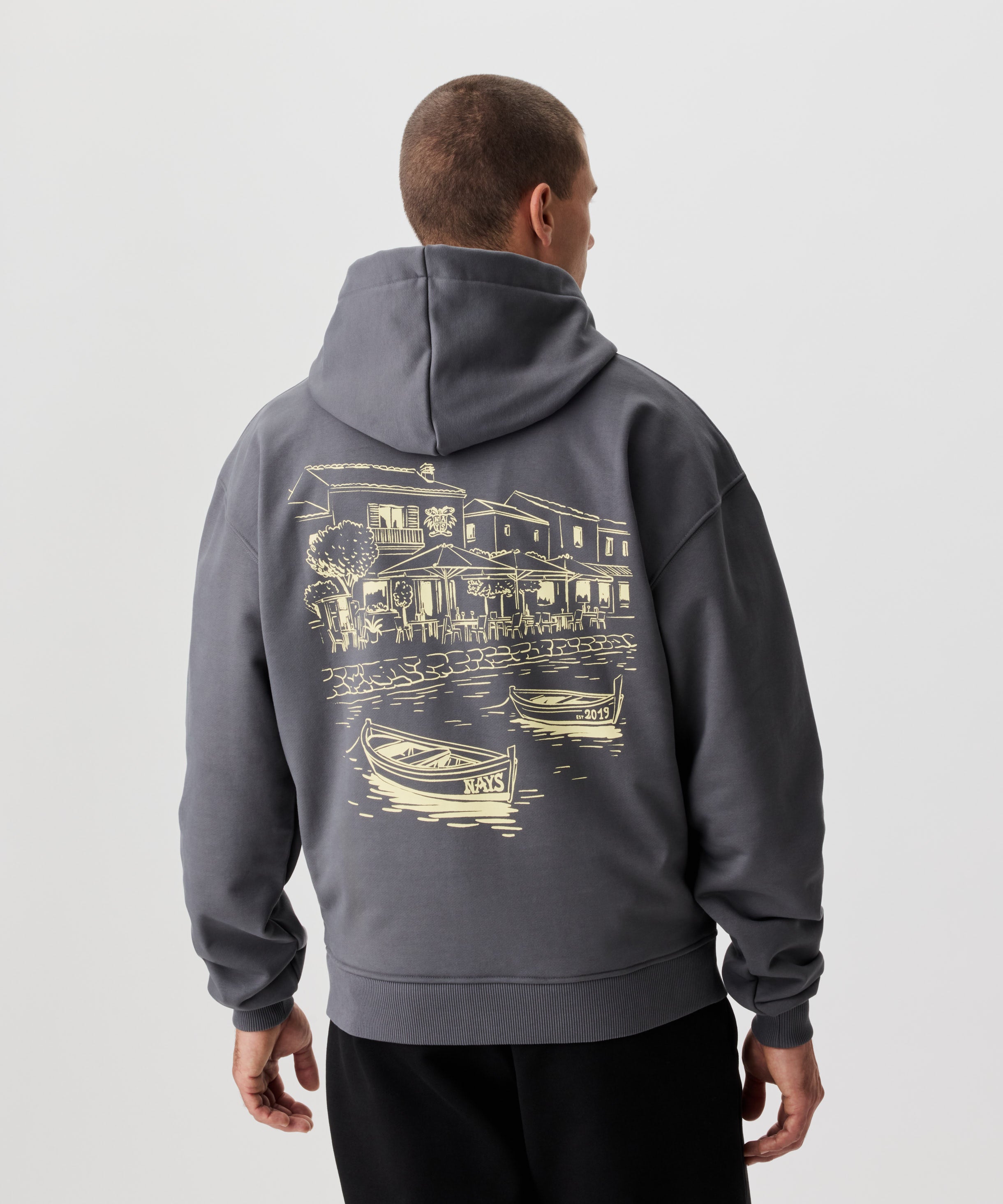 Rückansicht Mann im grauem Kapuzen Sweatshirt. Das Sweatshirt hat einen auffälligen Druck in gelb.