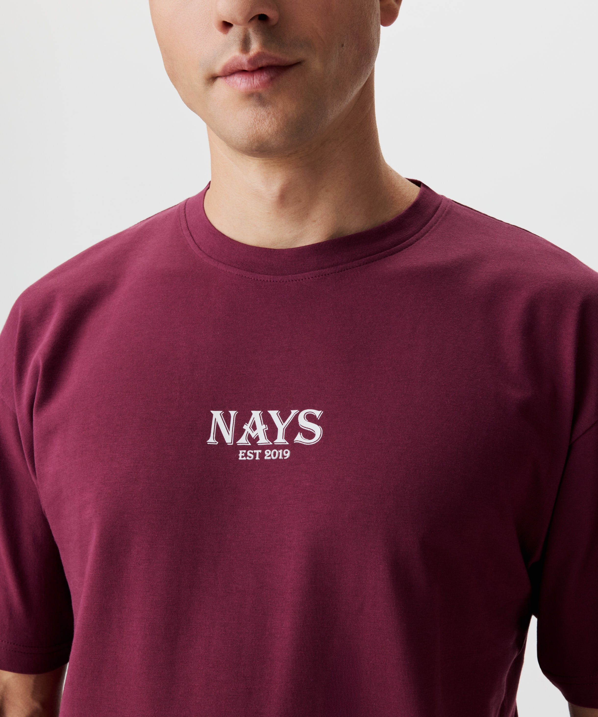 Frontansicht Mann im weinroten T-Shirt. Das T-Shirt hat einen mittig gesetztes Nays-Logo in weiß.