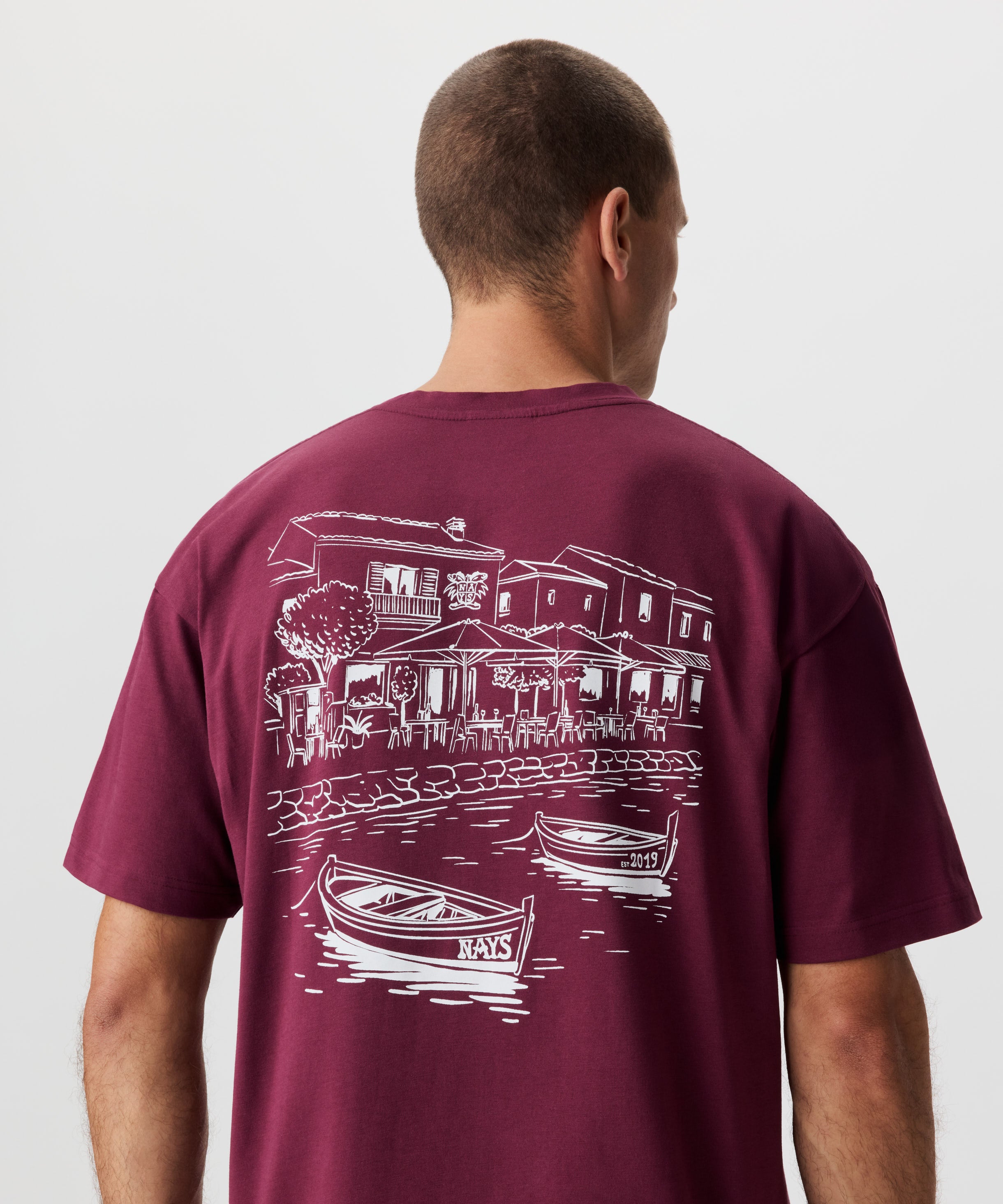 Rückansicht Mann im weinroten T-Shirt. Das T-Shirt hat einen auffälligen Druck in weiß.