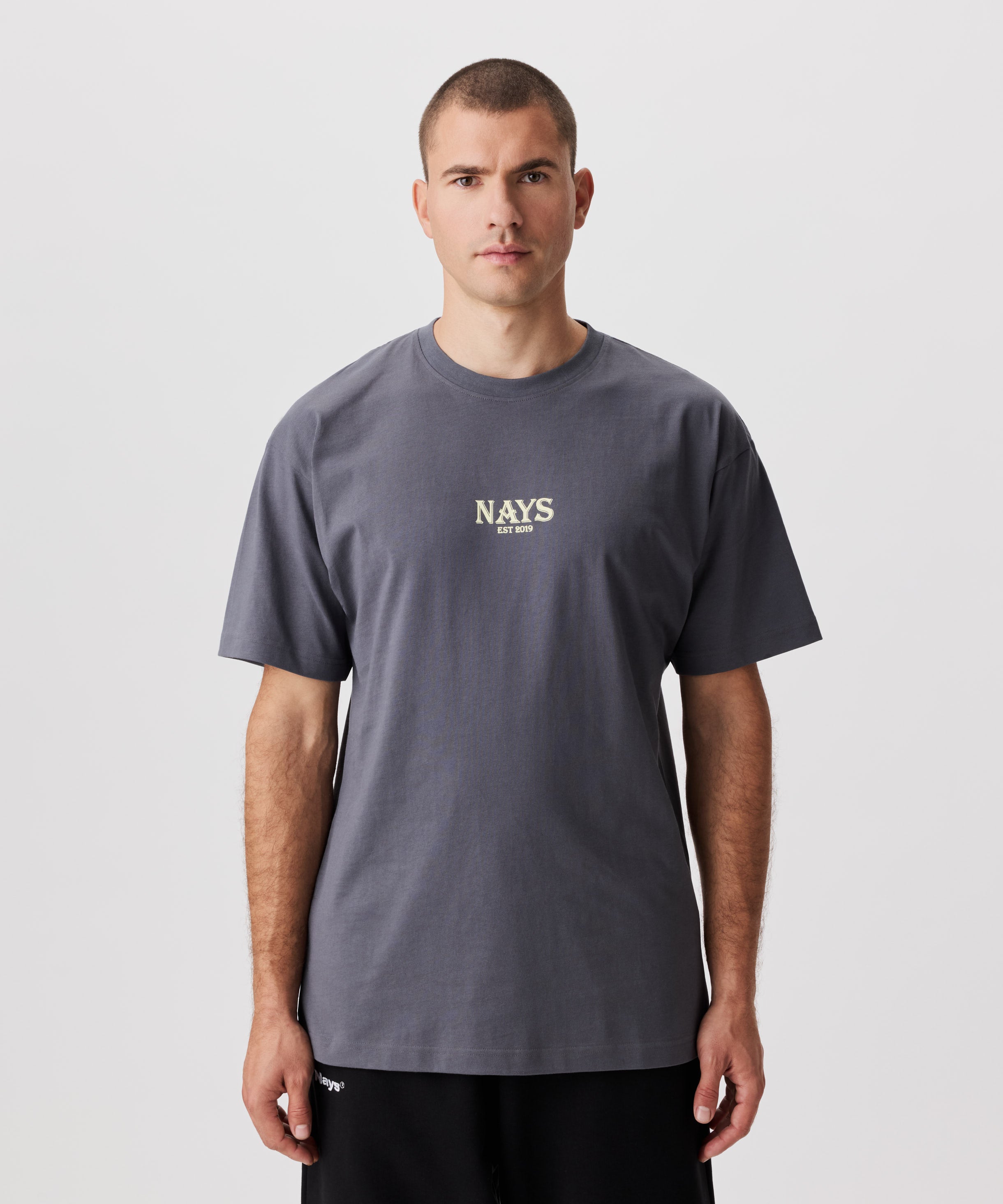 Frontansicht Mann im grauen T-Shirt. Das T-Shirt hat einen mittig gesetztes Nays-Logo in gelb.