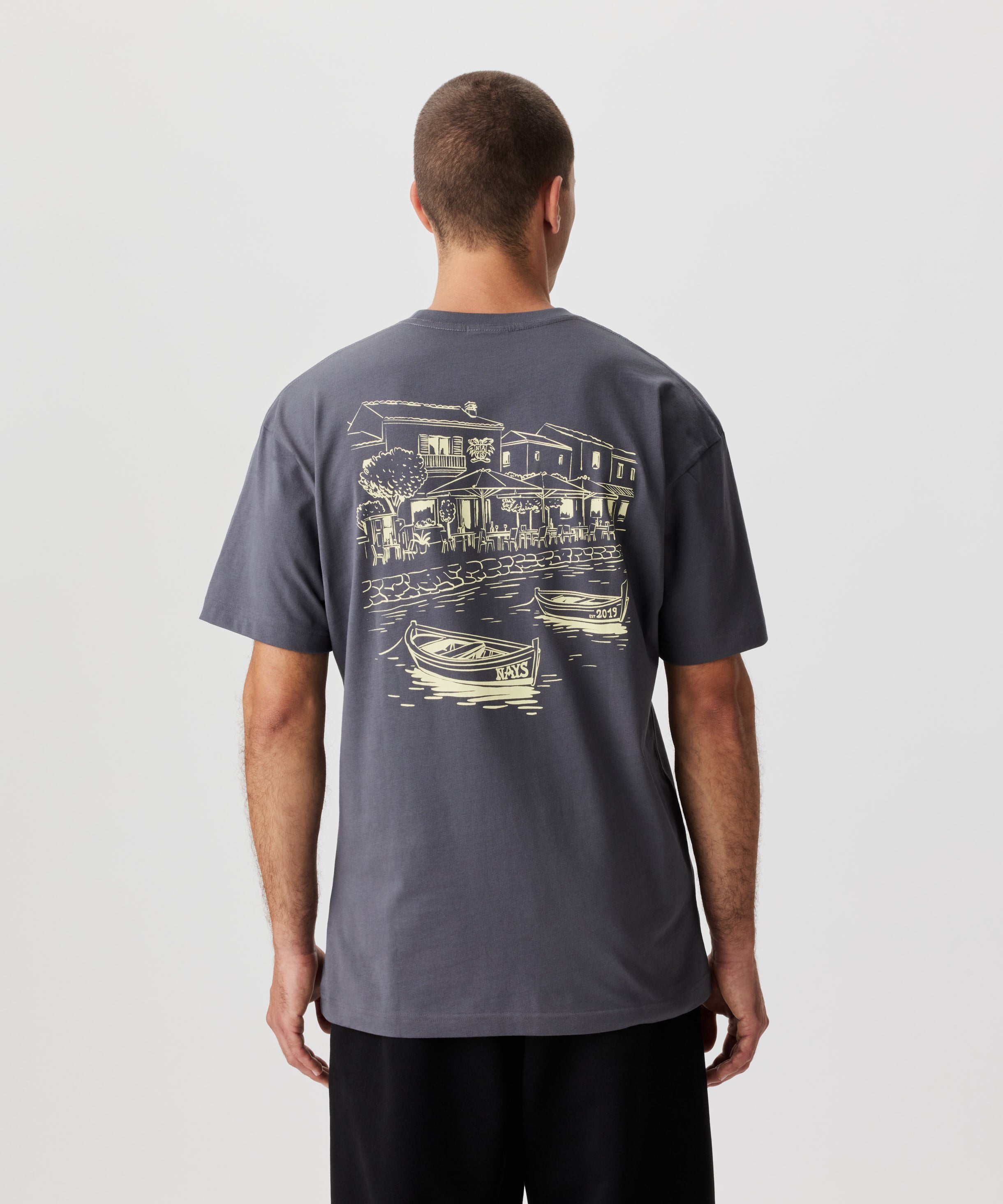 Rückansicht Mann im grauen T-Shirt. Das T-Shirt hat einen auffälligen Druck in gelb.