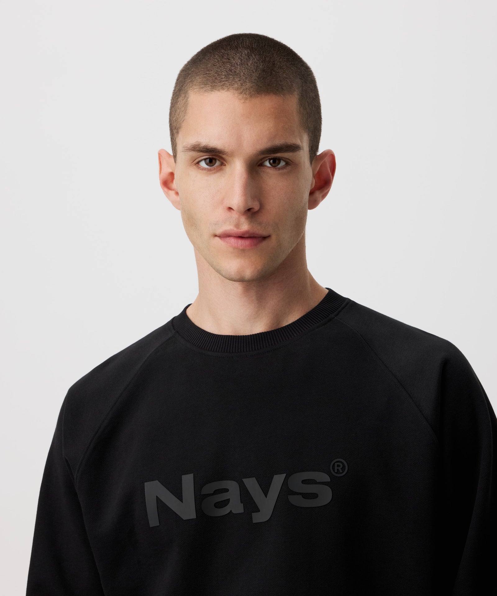 Auf dem Bild trägt ein Mann einen schwarzen Pullover. Gut zu erkennen ist ein großes, tonales Nays Logo auf der Brust. 