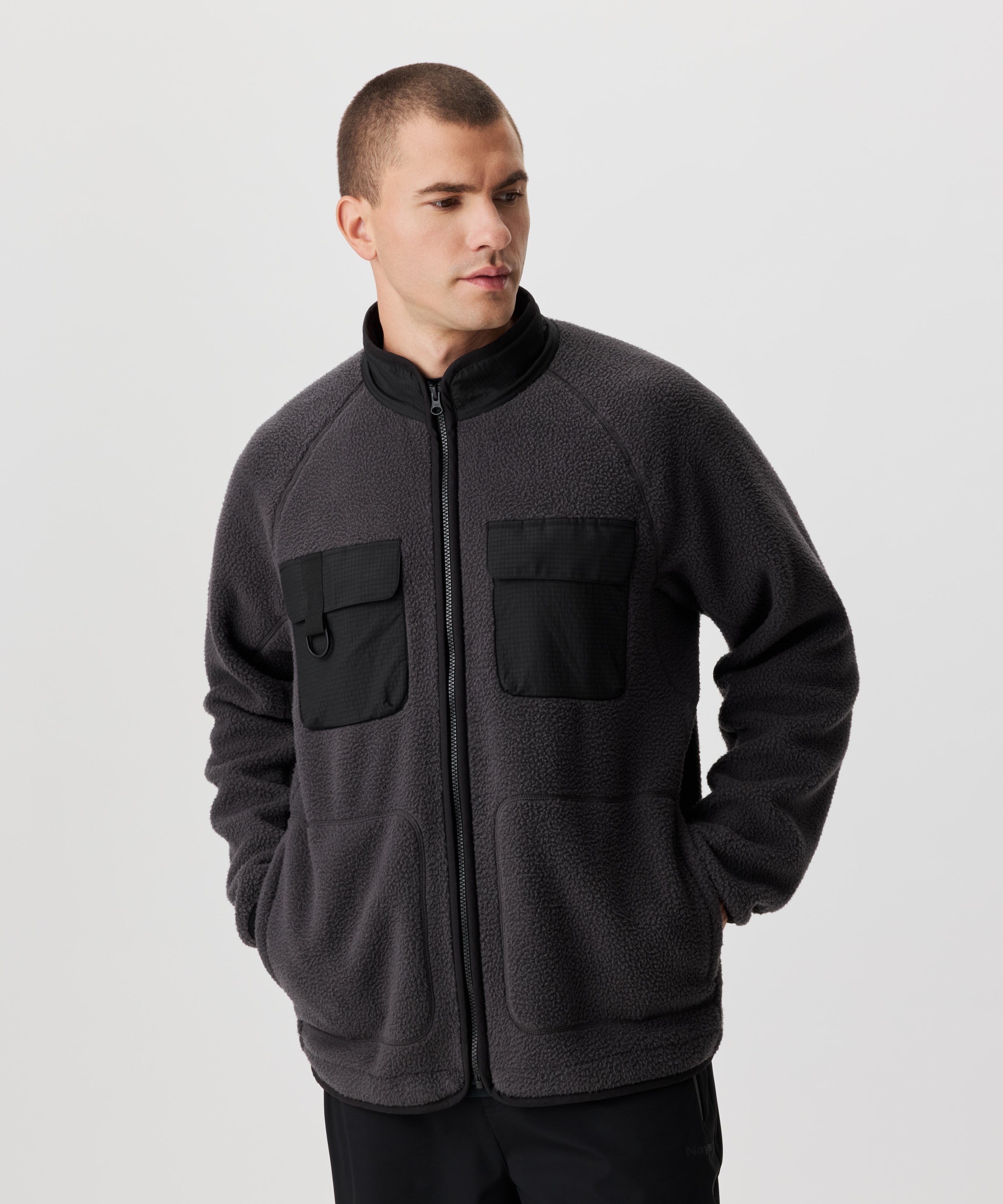 Frontansicht von einem Mann in dunkel-grauer Fleece-Jacke mit abgesetzten Kragen und Brusttaschen im schwarzen Ripstop. 