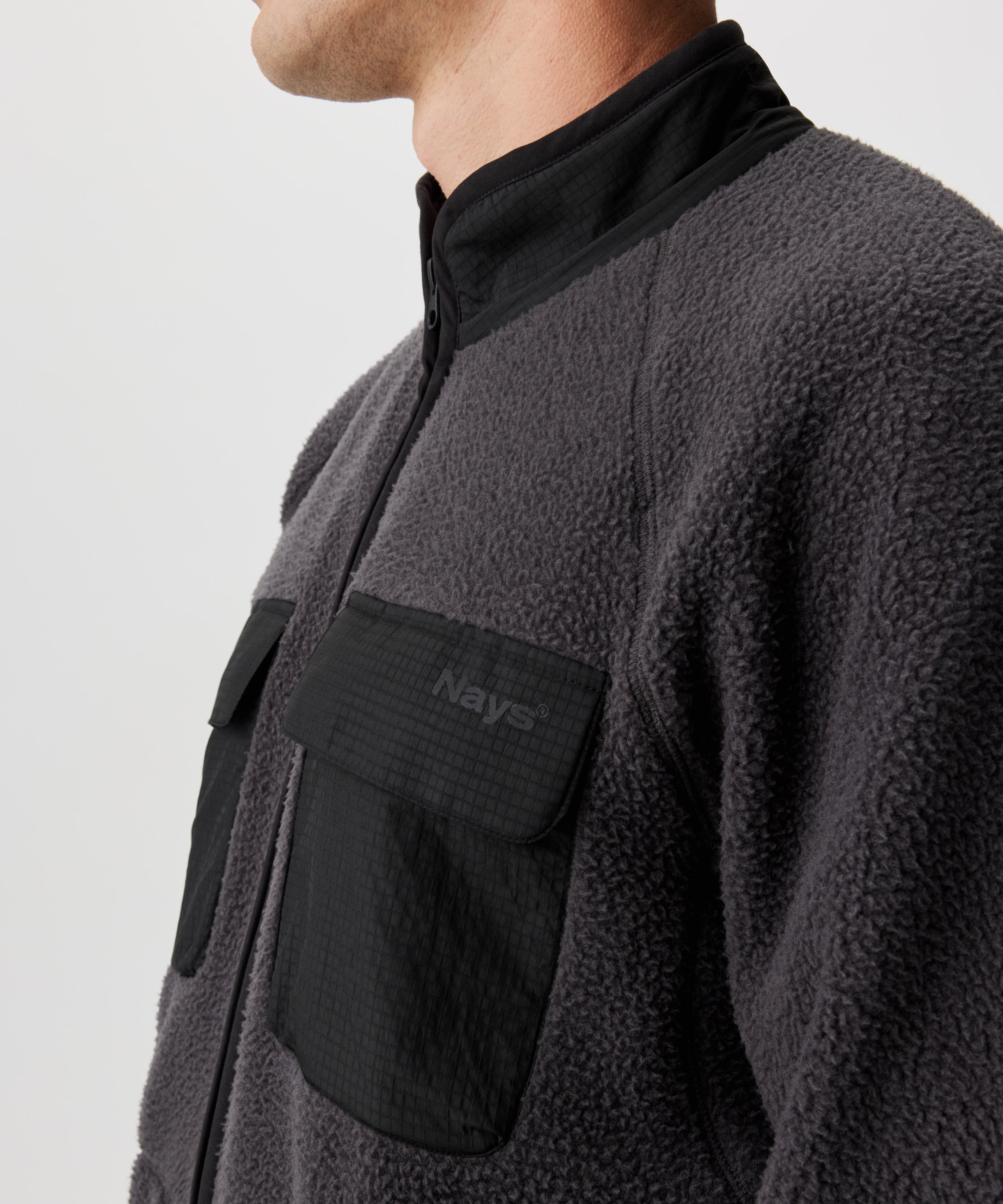 Ansicht von einem Mann in dunkel-grauer Fleece-Jacke mit abgesetzten Kragen und Brusttaschen im schwarzen Ripstop. 