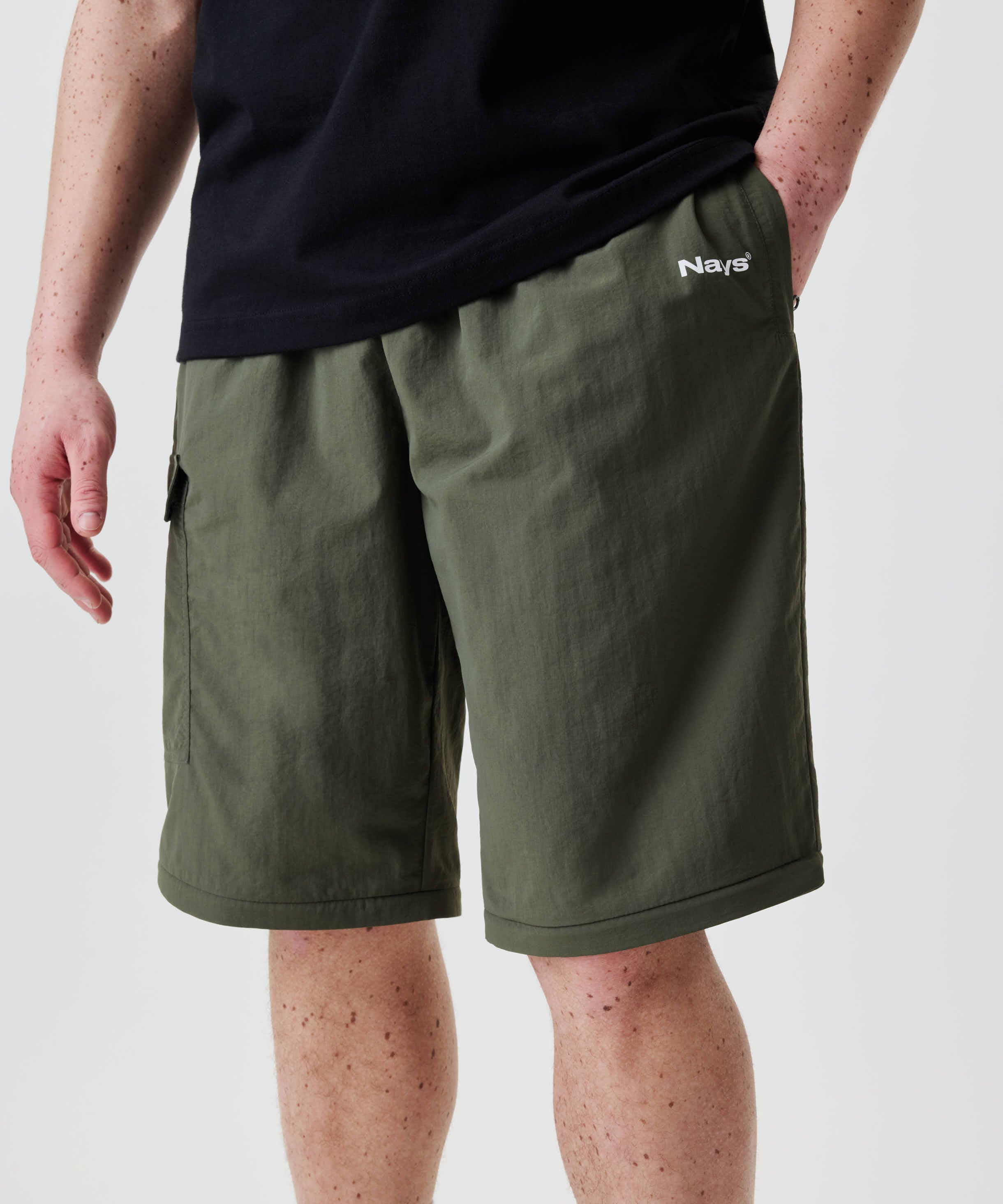 Nays Lightweight Zip Off Pants in Kniehöhe mit seitlichen Taschen und Nays-Logo; Hand in Tasche, schwarze T-Shirt. Ideal für flexible Nutzung durch abnehmbare Beine.