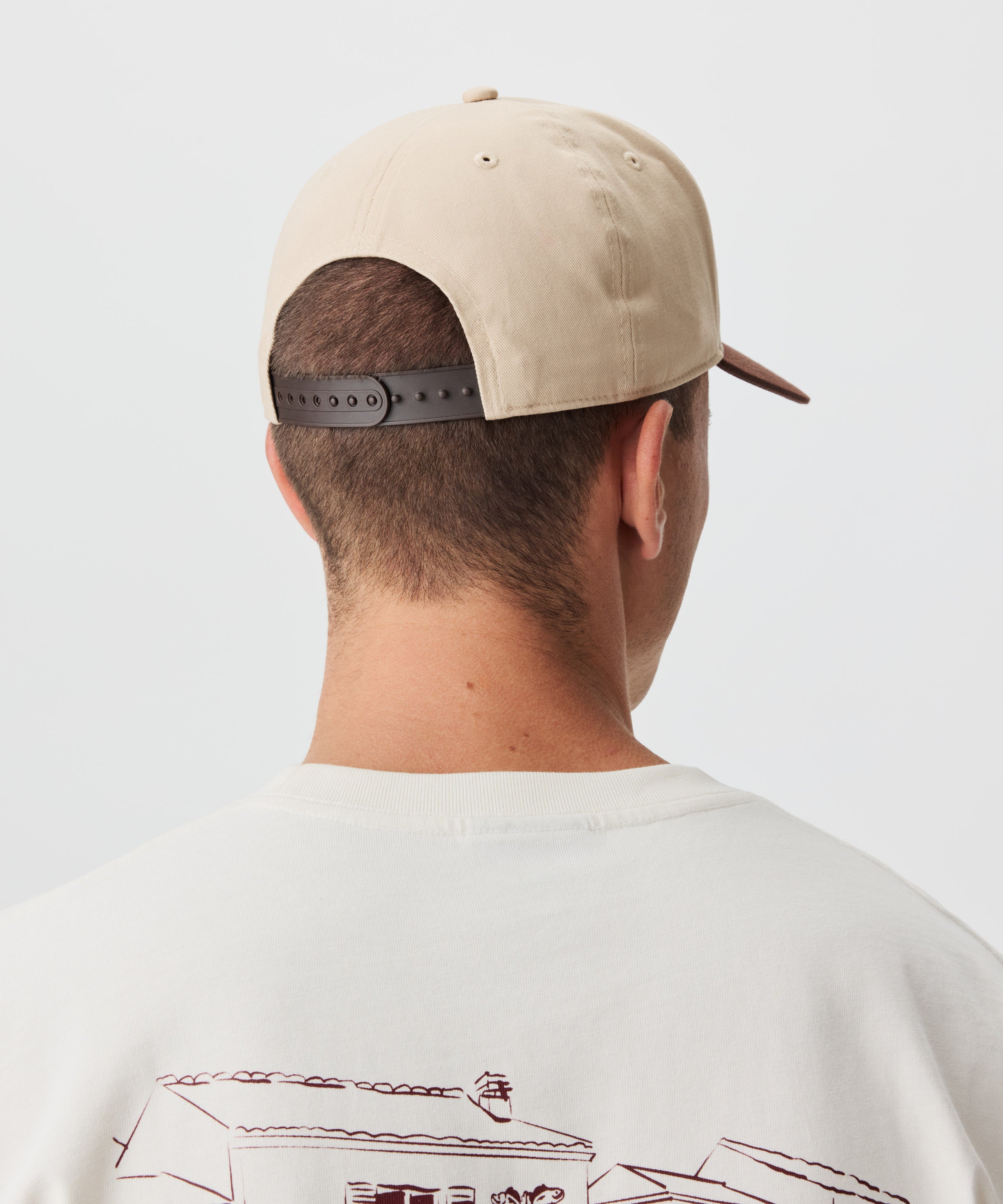 Rückanischt Mann mit Cap. Die Cap ist beige und hat einen braunen Schirm.