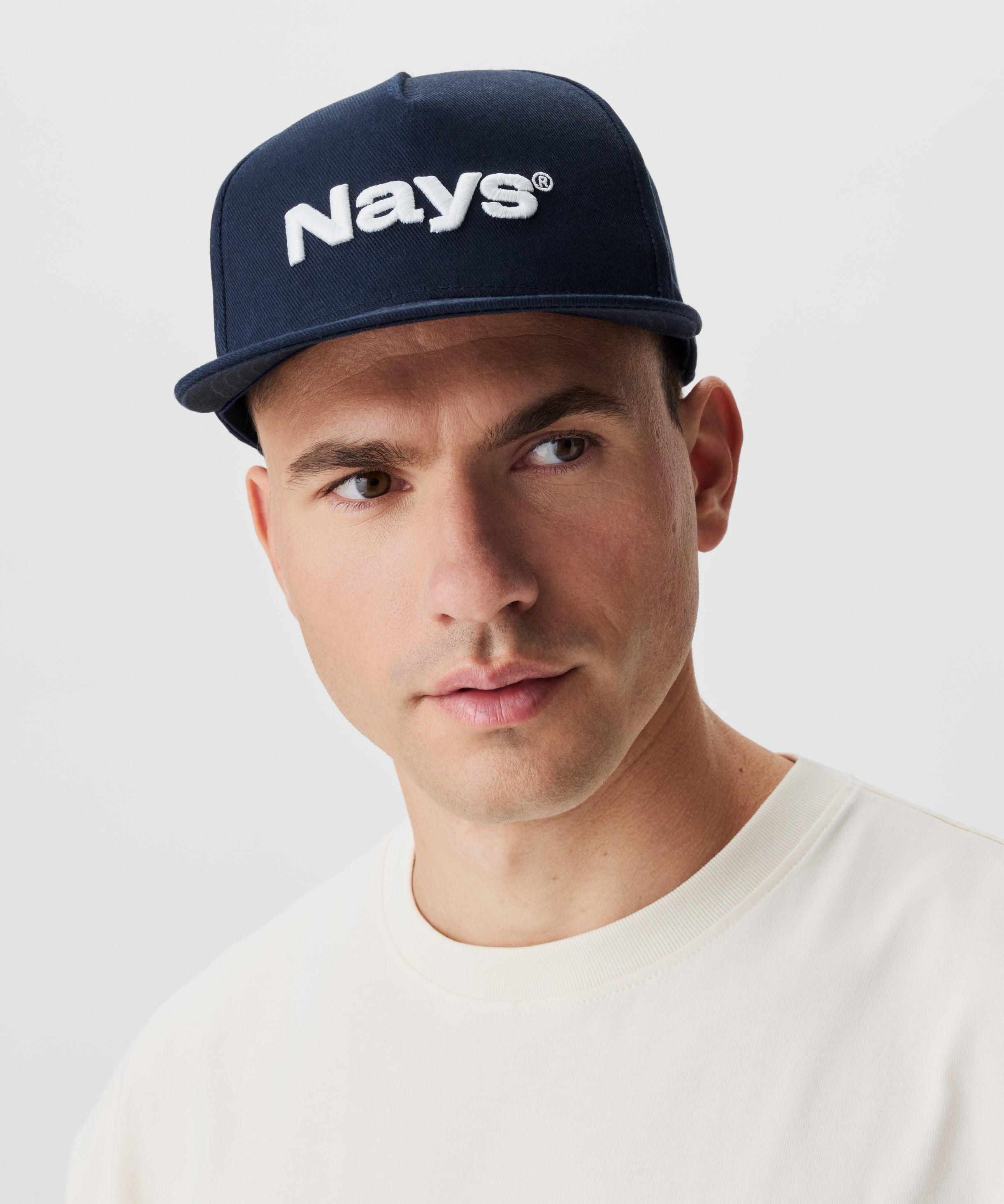 Frontansicht Mann mit Cap. Die Cap ist blau mit einem weißen Nays-Logo Strick.
